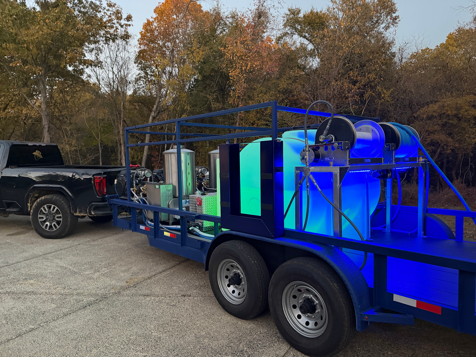 A dark truck tows a blue industrial trailer featuring large, brightly lit turquoise and blue translucent tanks.