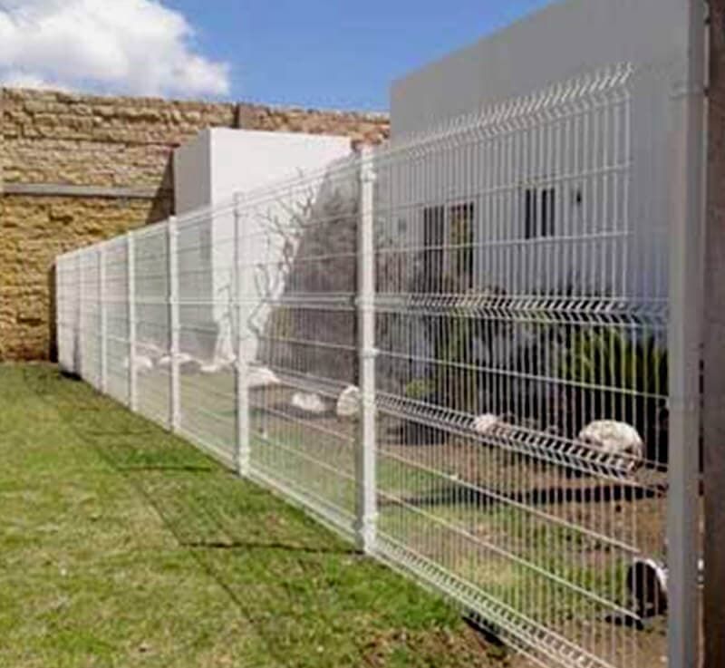 Una valla blanca rodea un exuberante jardín verde frente a una casa.