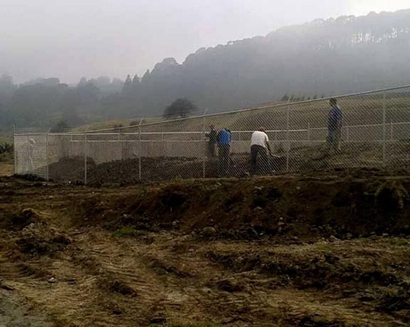 Un grupo de personas está trabajando en un campo fangoso detrás de una valla.