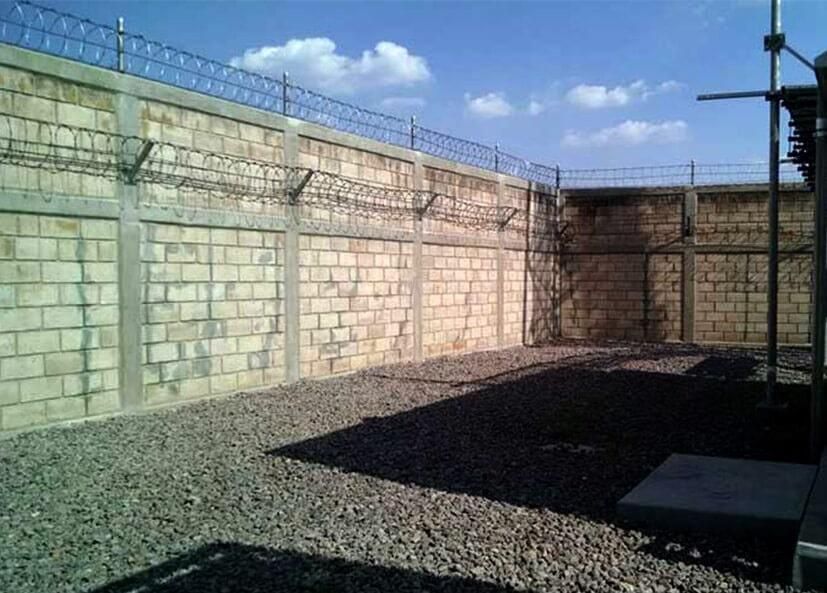 Una pared de ladrillos con alambre de púas rodea un área de grava