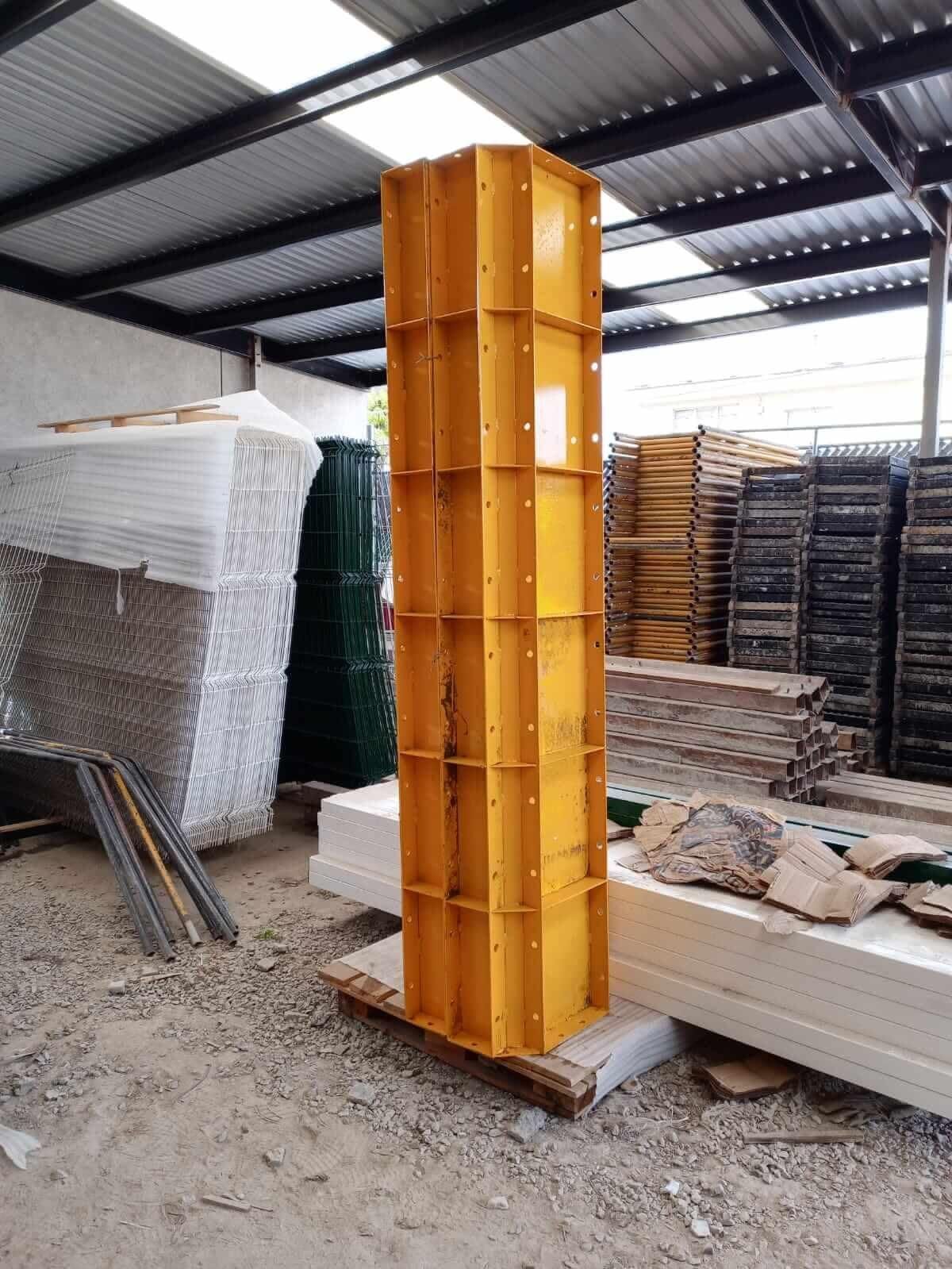 Un pilar amarillo se encuentra en un almacén junto a una pila de andamios.