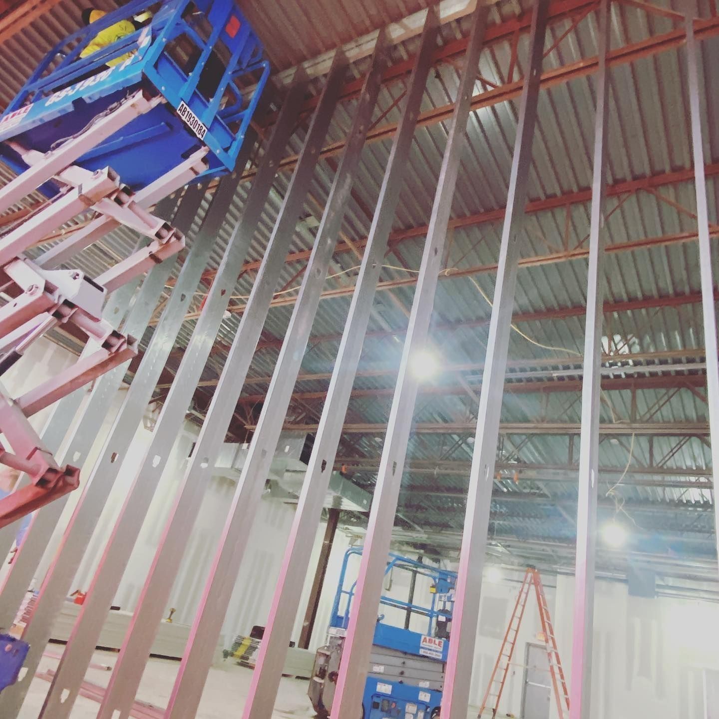 Construction site with metal framing, blue lift, and high ceiling.