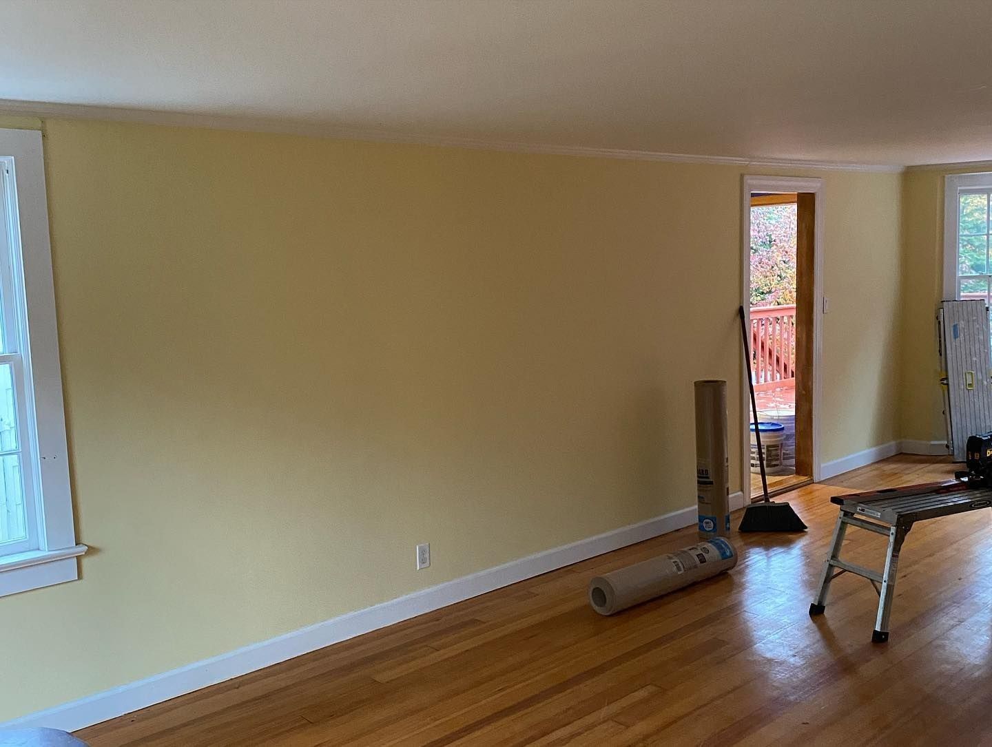 Yellow-painted interior room with hardwood floors, a door to a deck, and rolled up carpeting.