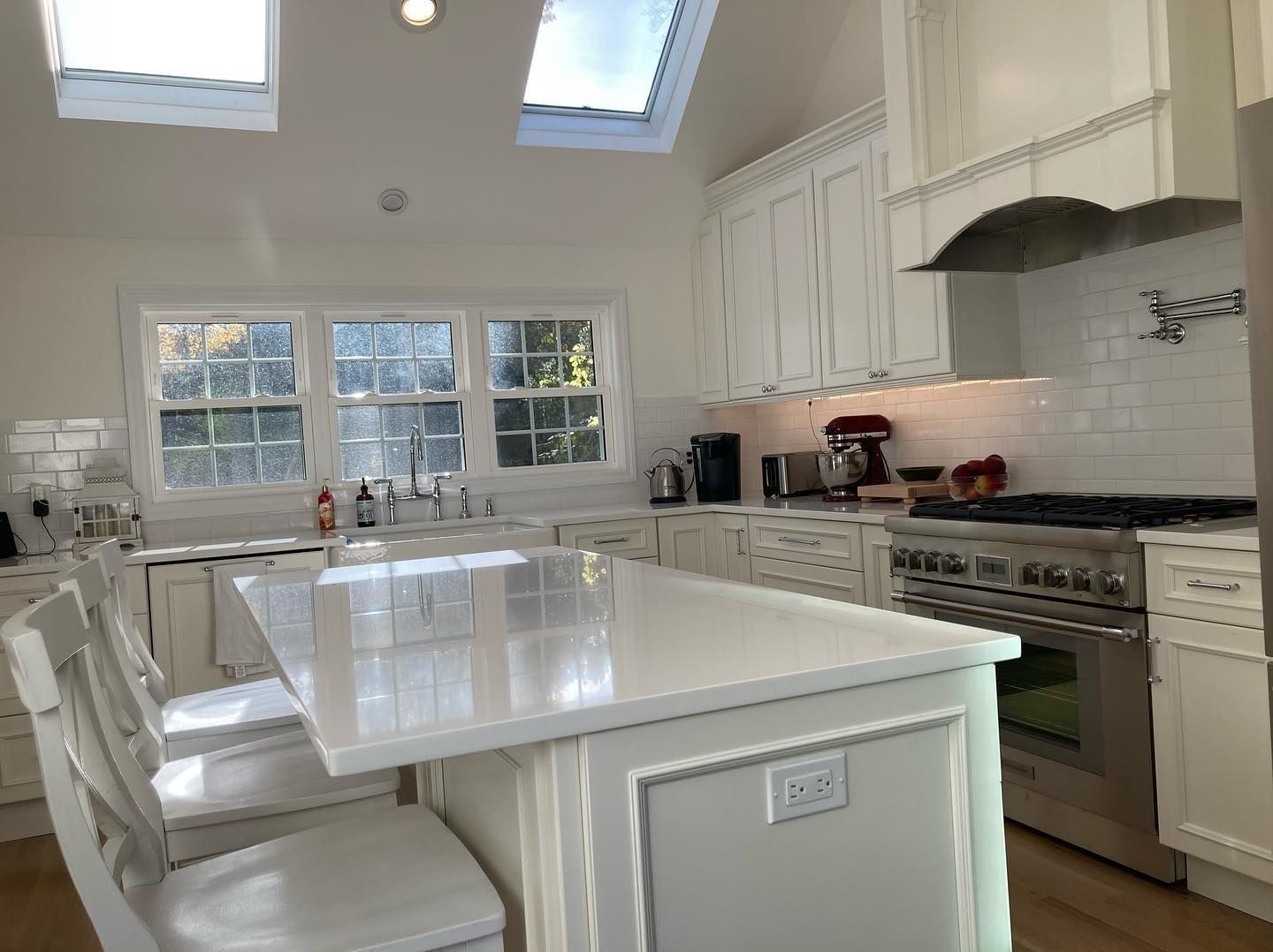White kitchen with island, cabinets, skylights, and stainless steel appliances.