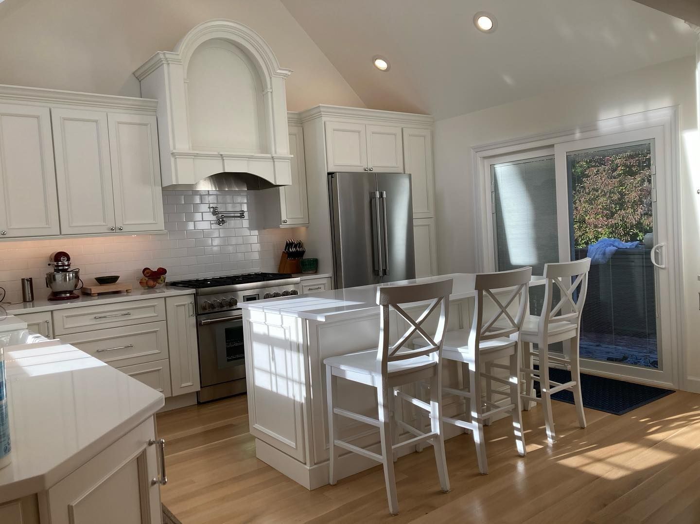 White kitchen with island and bar stools, stainless steel appliances, and sliding glass door.