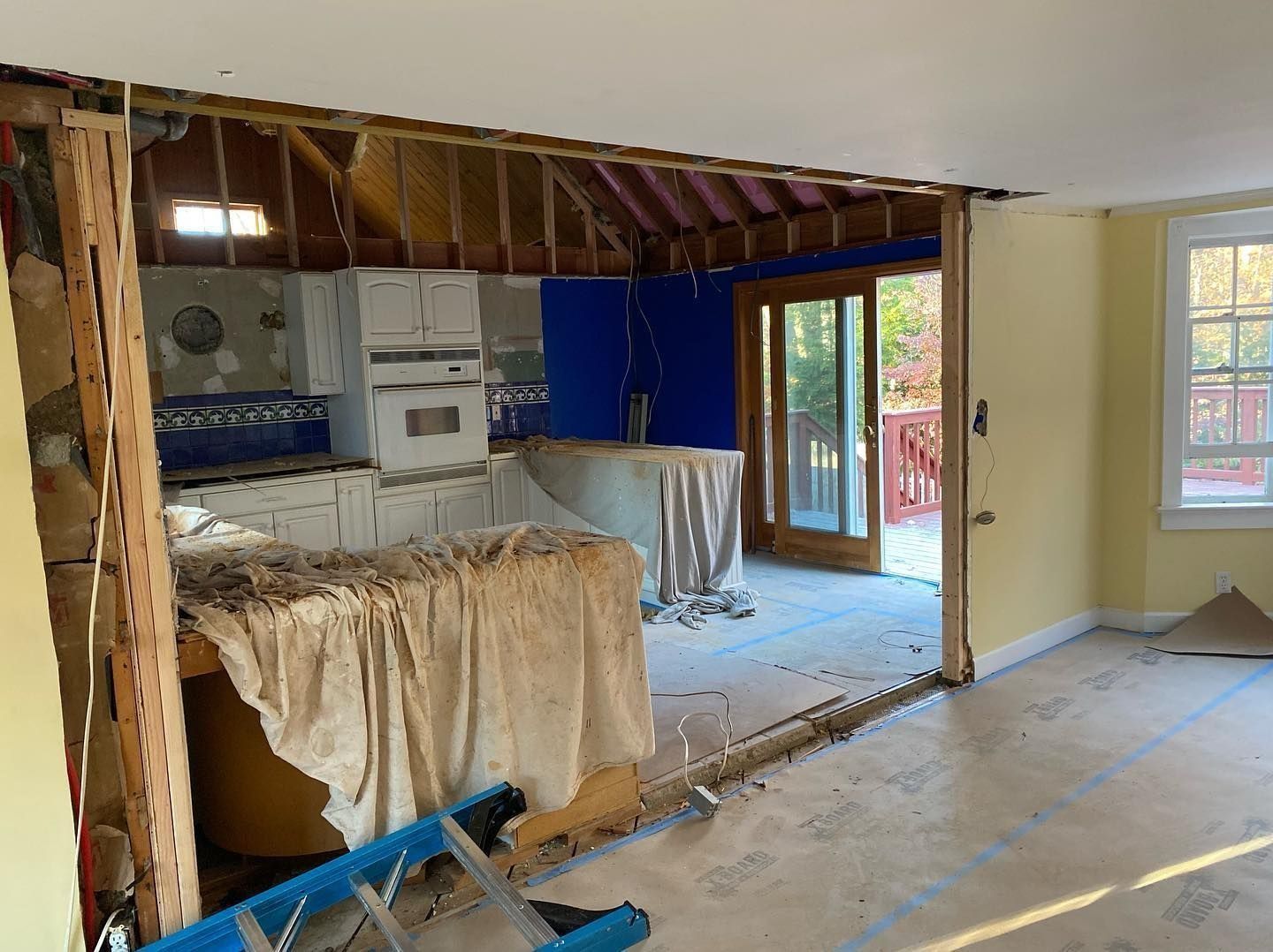 Kitchen under construction: doorway opening, partially demolished walls, cabinets, blue paint, and patio door.