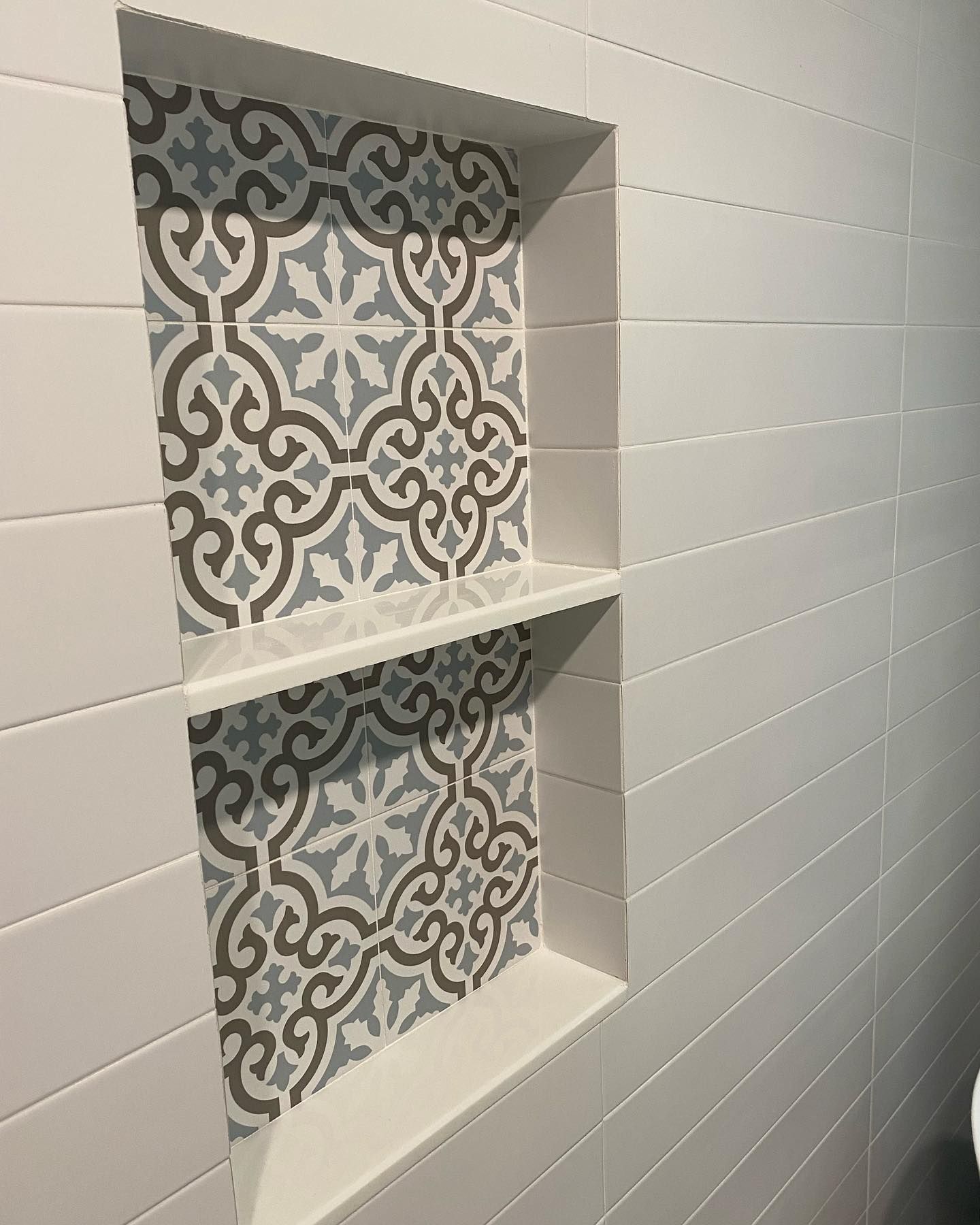 Recessed white tiled shower niche with patterned tile back and shelf.