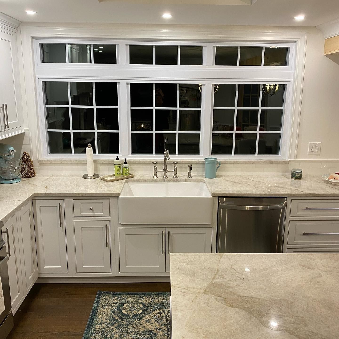 White kitchen with a farmhouse sink under a large window. Granite countertops and stainless steel appliances.