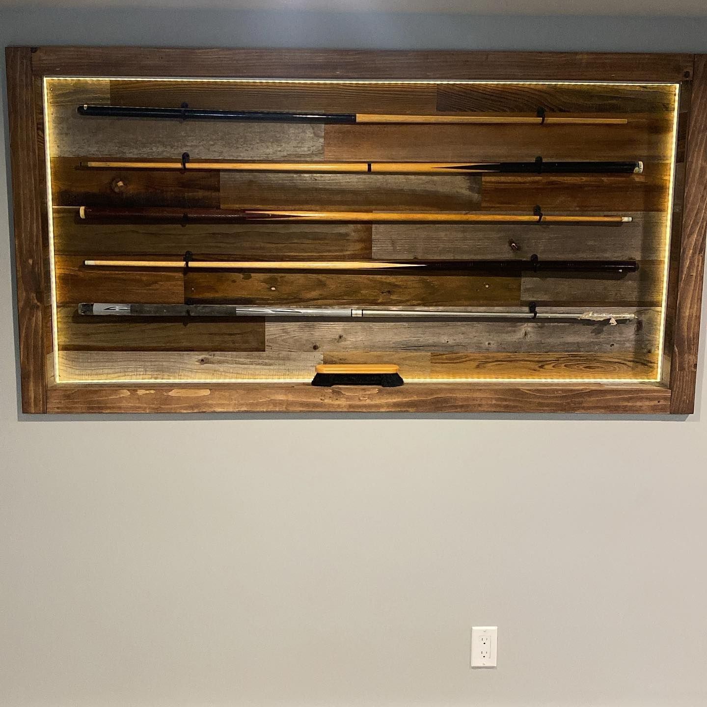 Wooden display case with pool cues and led lighting, mounted on a grey wall.