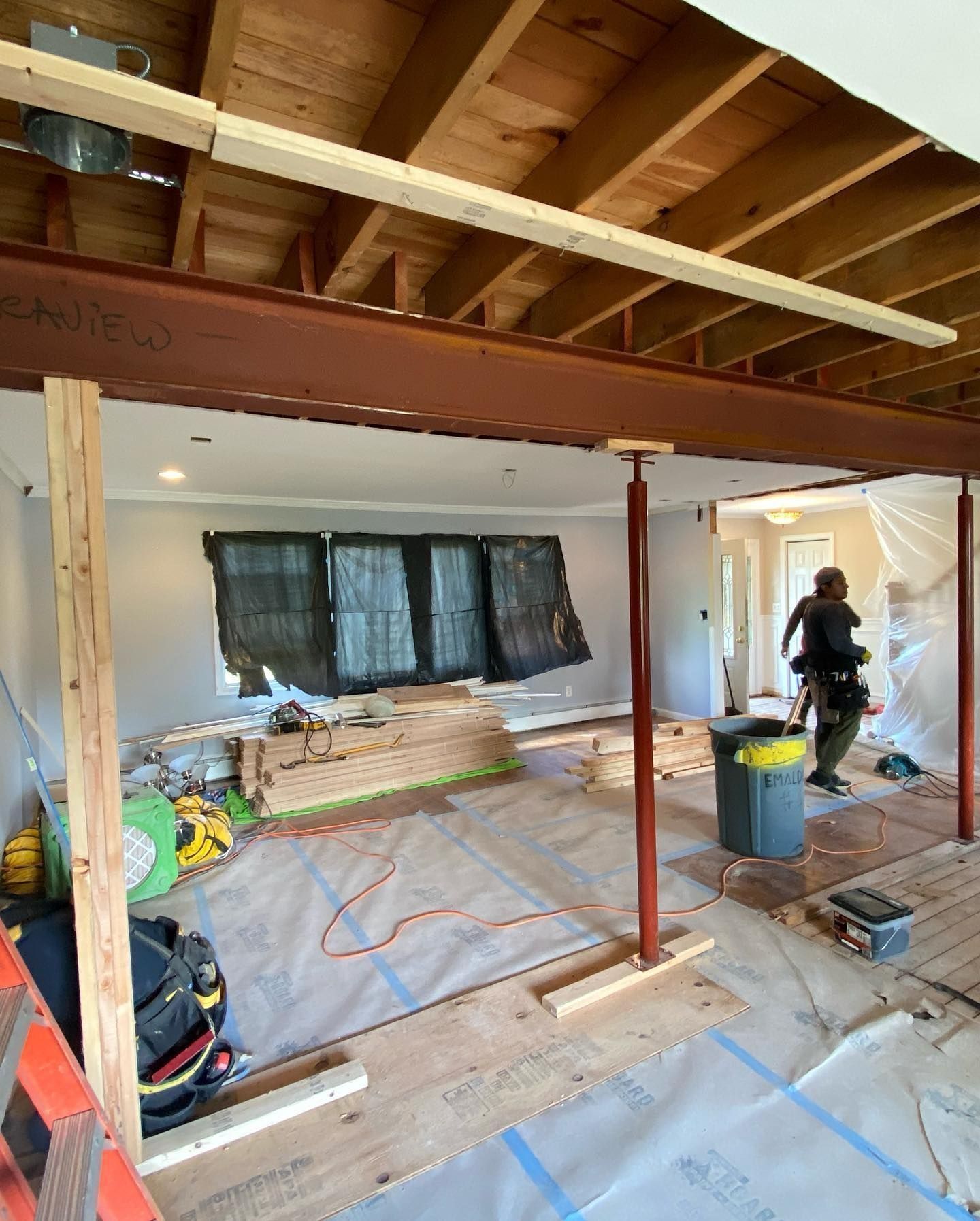 Interior renovation: a large brown steel beam supported by red jacks. A worker is in the doorway.