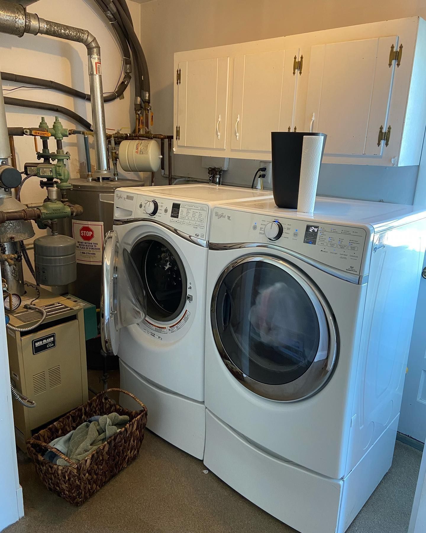 A washer and dryer set in a laundry room, with a basket and storage cabinets.