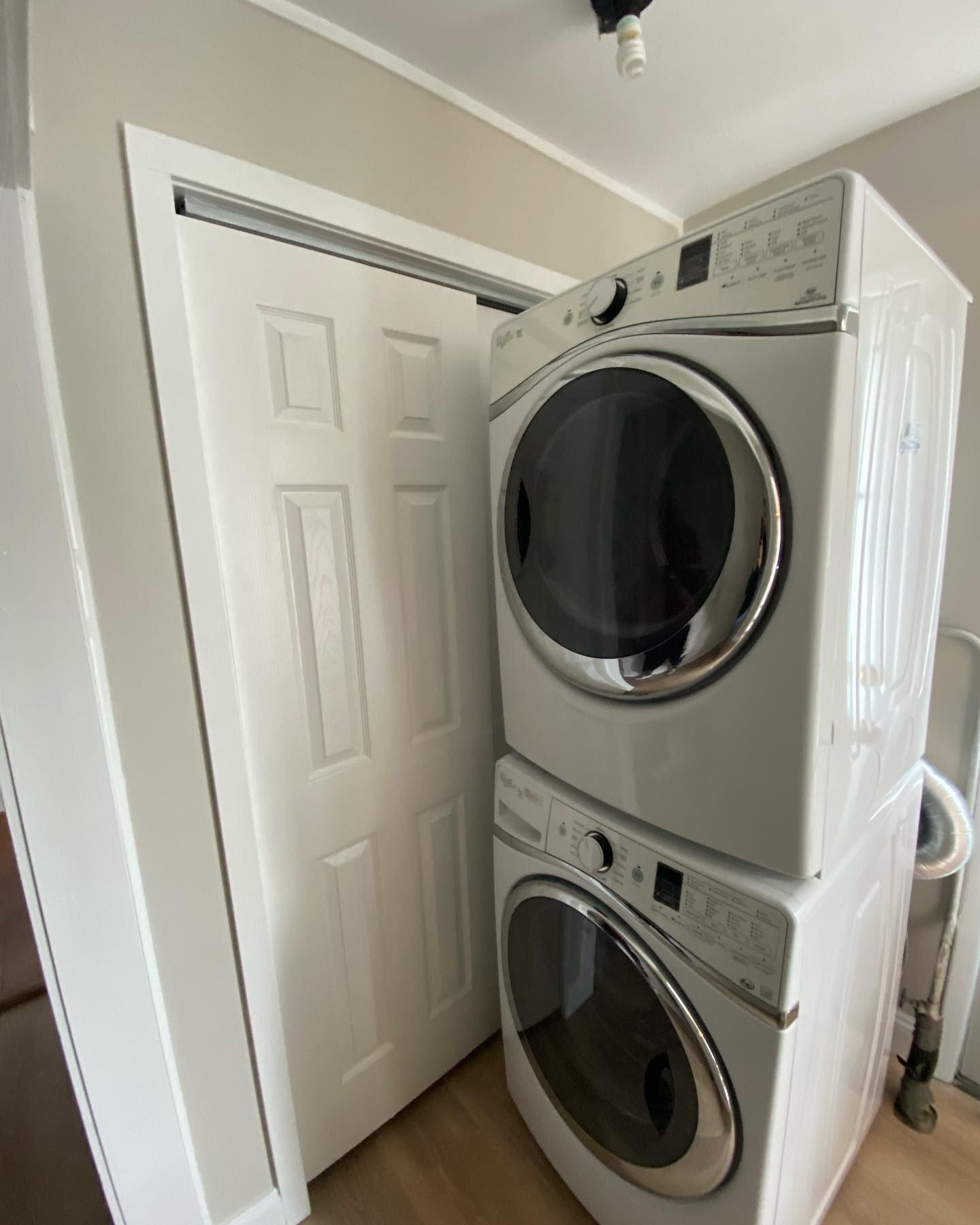 Stacked white washer and dryer in a laundry room, next to a closed white door.