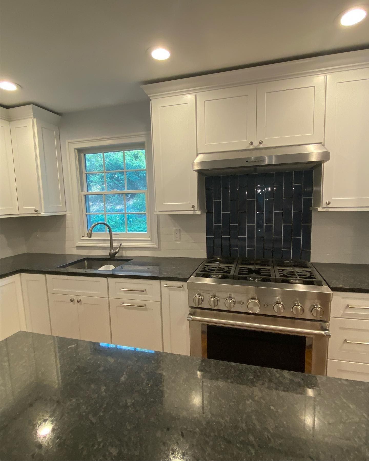 White kitchen with stainless steel appliances, dark countertops, and a dark blue tiled backsplash.