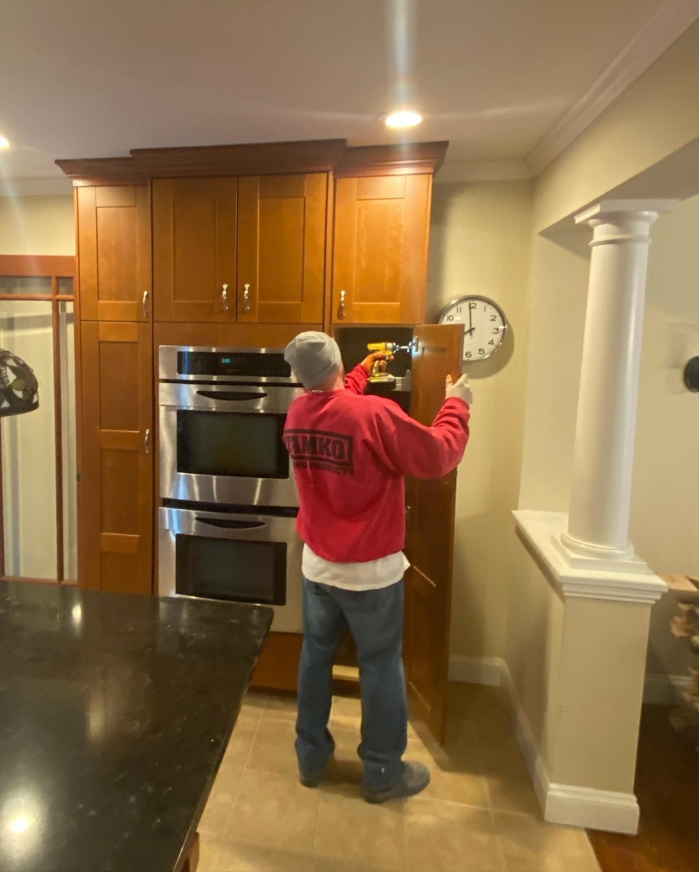 Person installing kitchen cabinet door near double oven and clock.