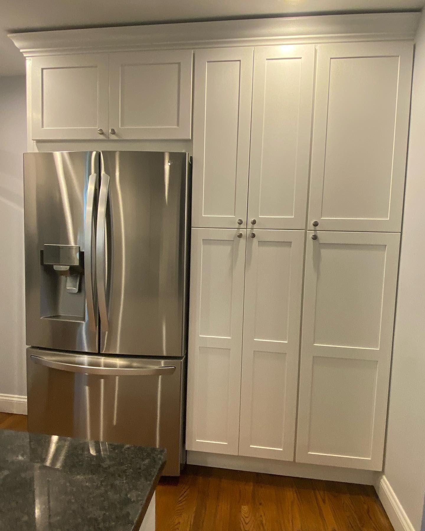 Stainless steel refrigerator and white pantry cabinets in a kitchen, with wood floors.