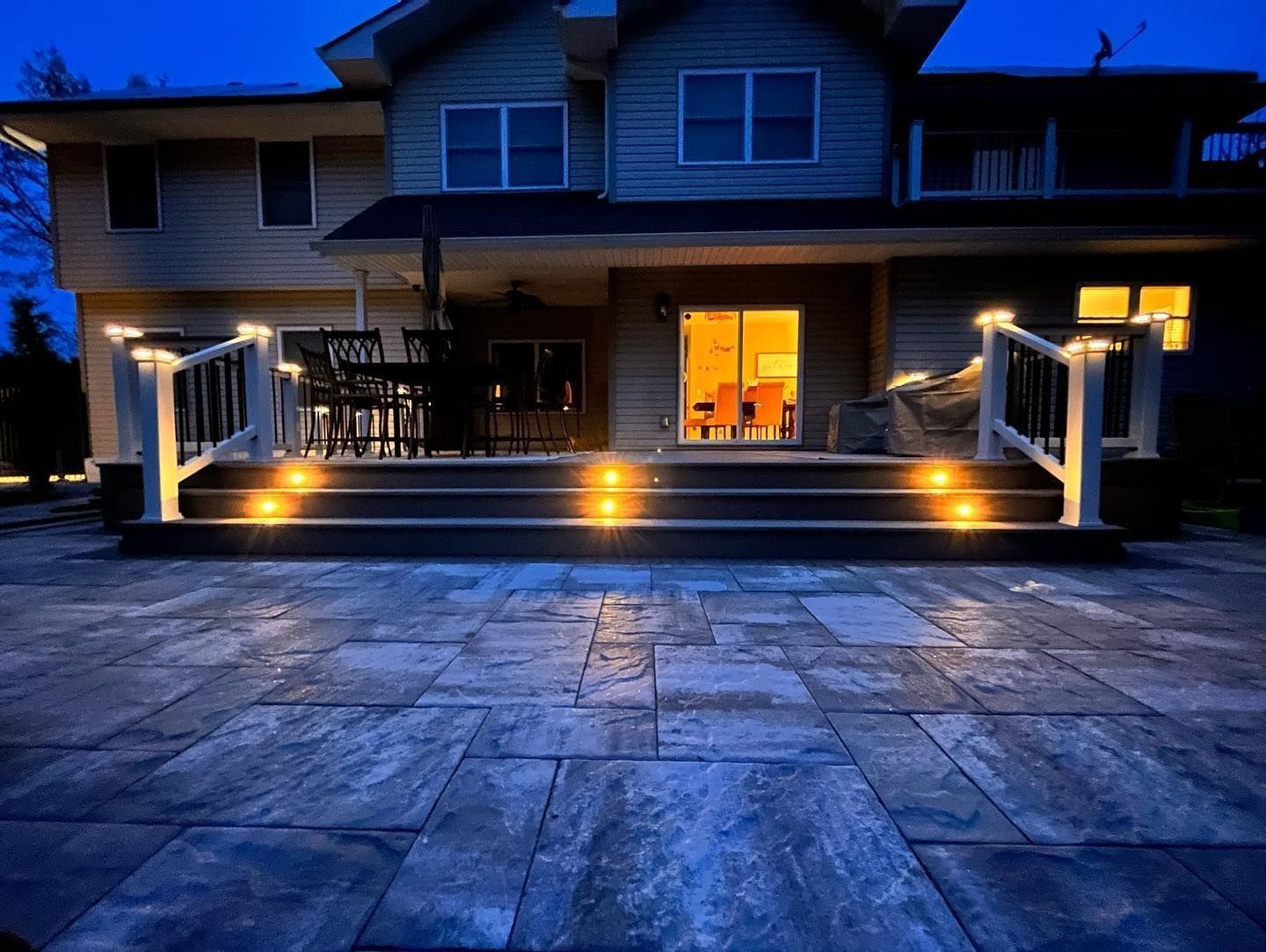 Night view of a house with lit patio steps and railings, stone patio, and lights inside.