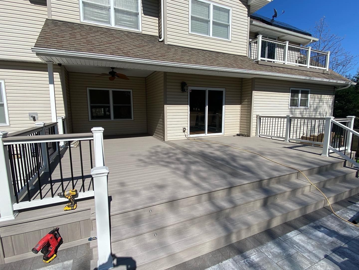 Elevated deck attached to a two-story house with railings. Gray composite decking, sliding door, white trim, sunny day.