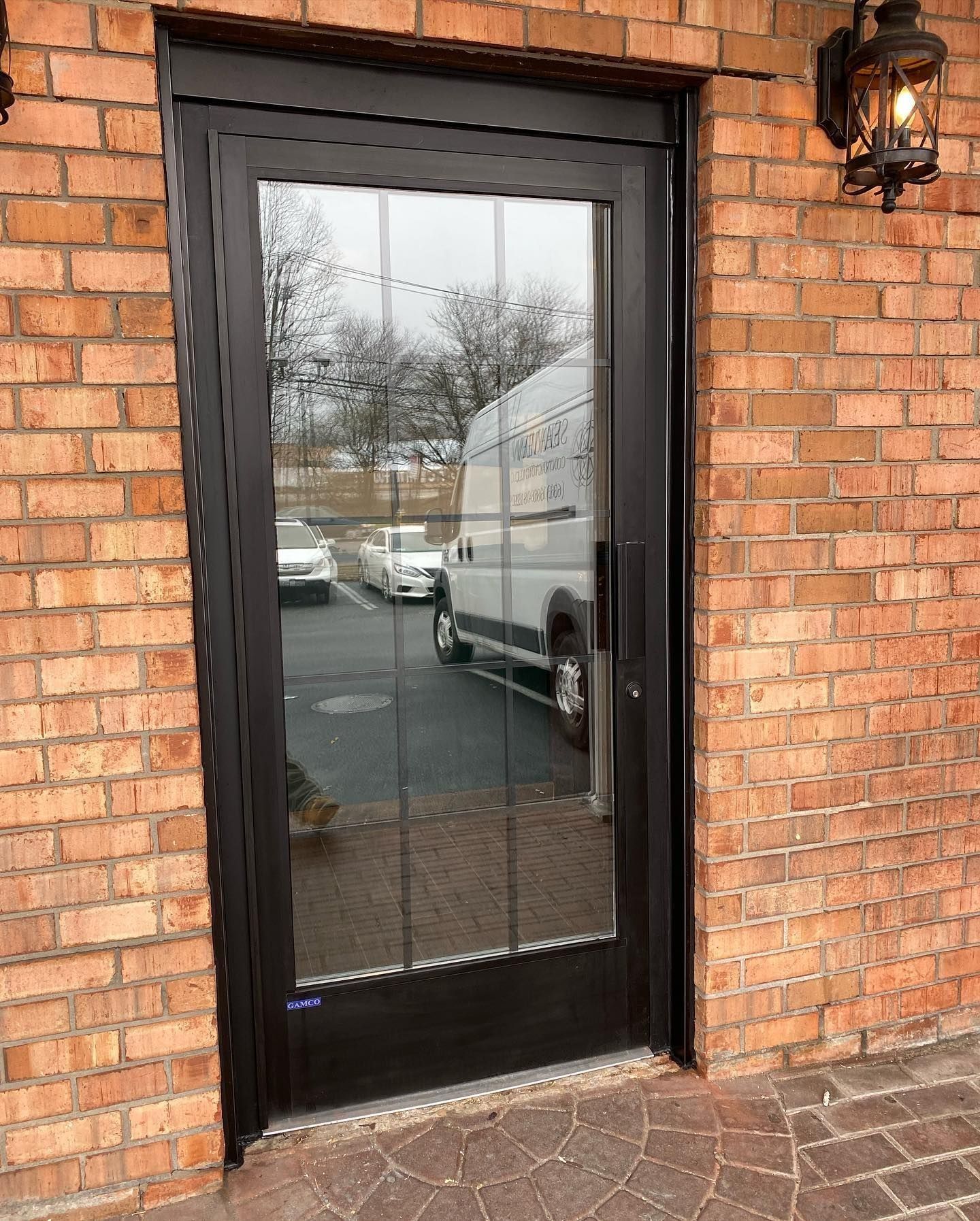 Black glass door with grid, set in brick wall, reflecting parked vehicles.