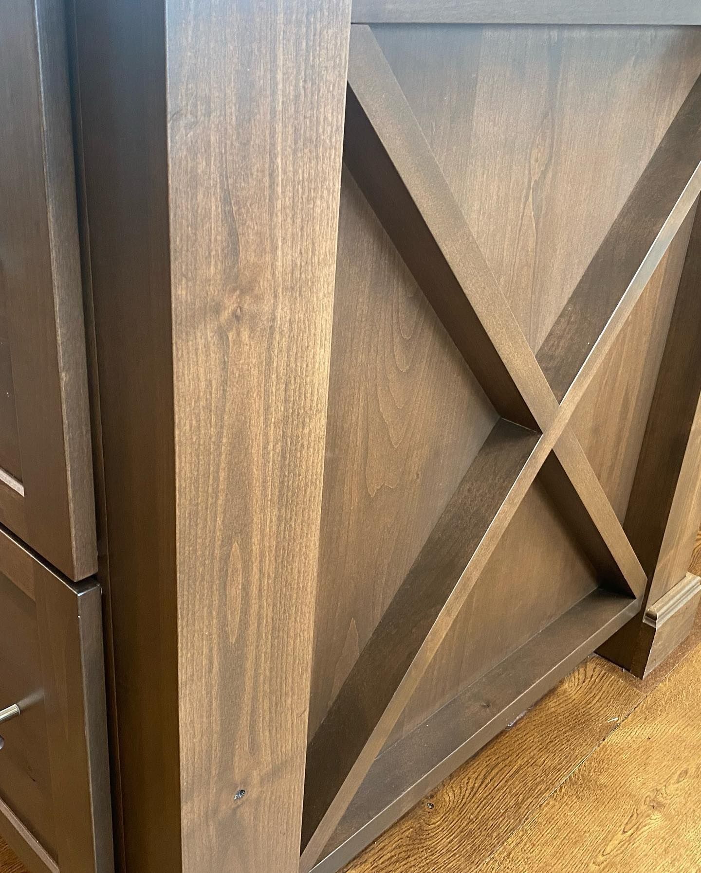 Wooden cabinet side with an X-shaped design, stained brown, on a wood floor.