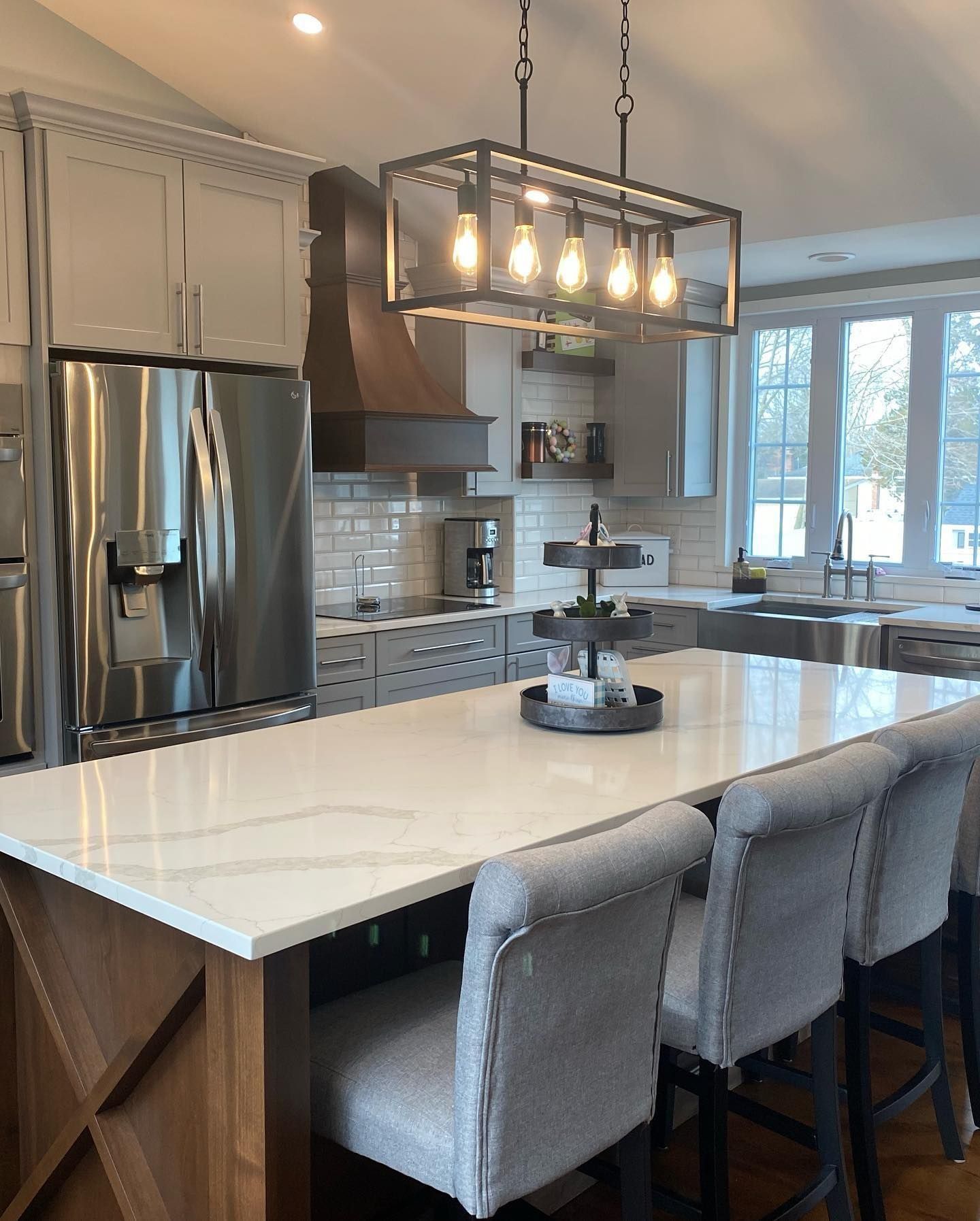 Modern kitchen with island, seating, and overhead light fixture. Stainless steel appliances and white countertops.