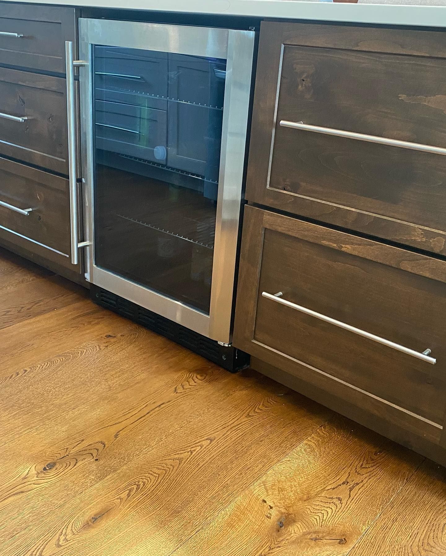 Built-in wine refrigerator between dark wood cabinets, with stainless steel accents and hardwood flooring.