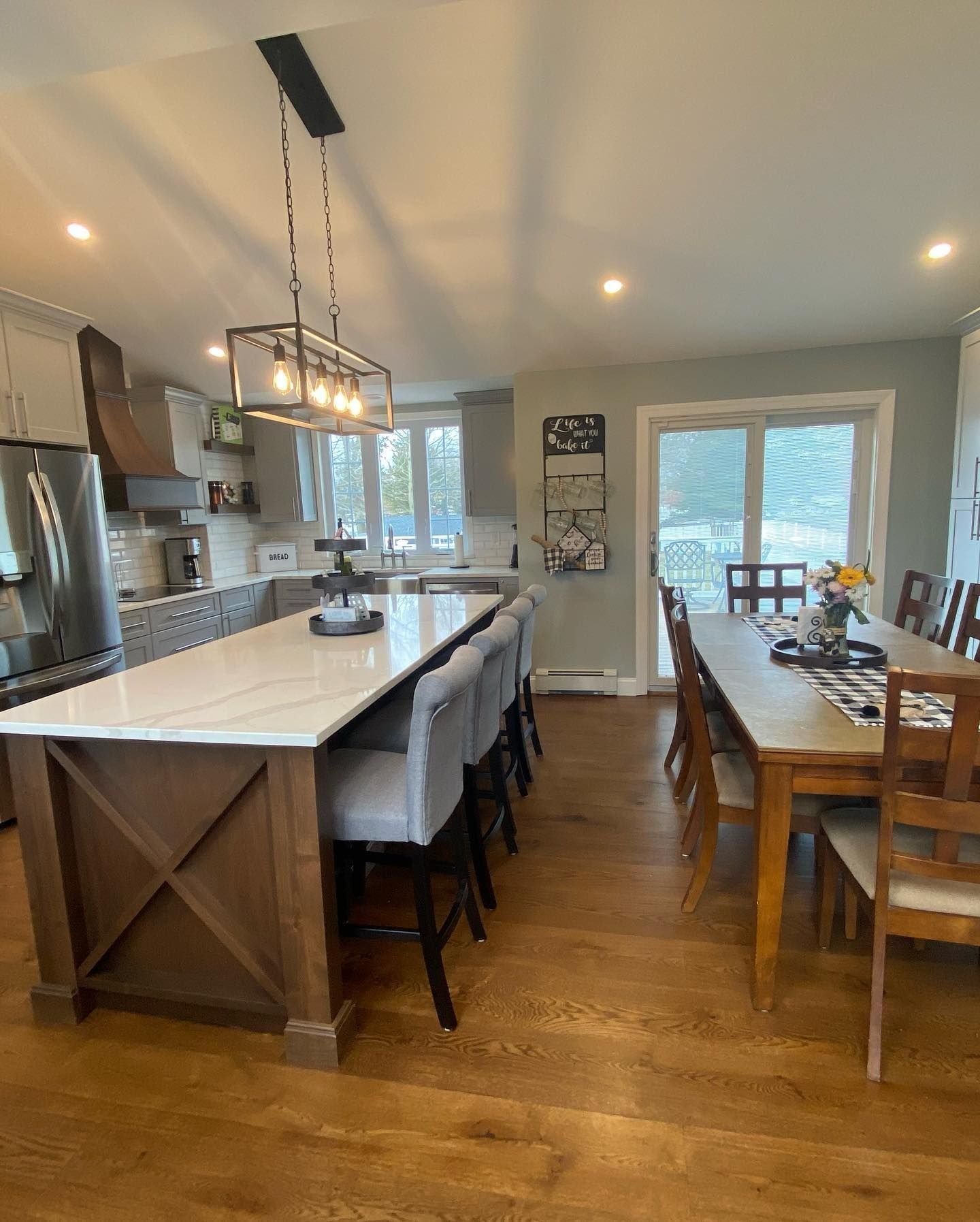 Kitchen with a large island, seating, and a dining table. Wooden floors, gray walls, and bright lighting.