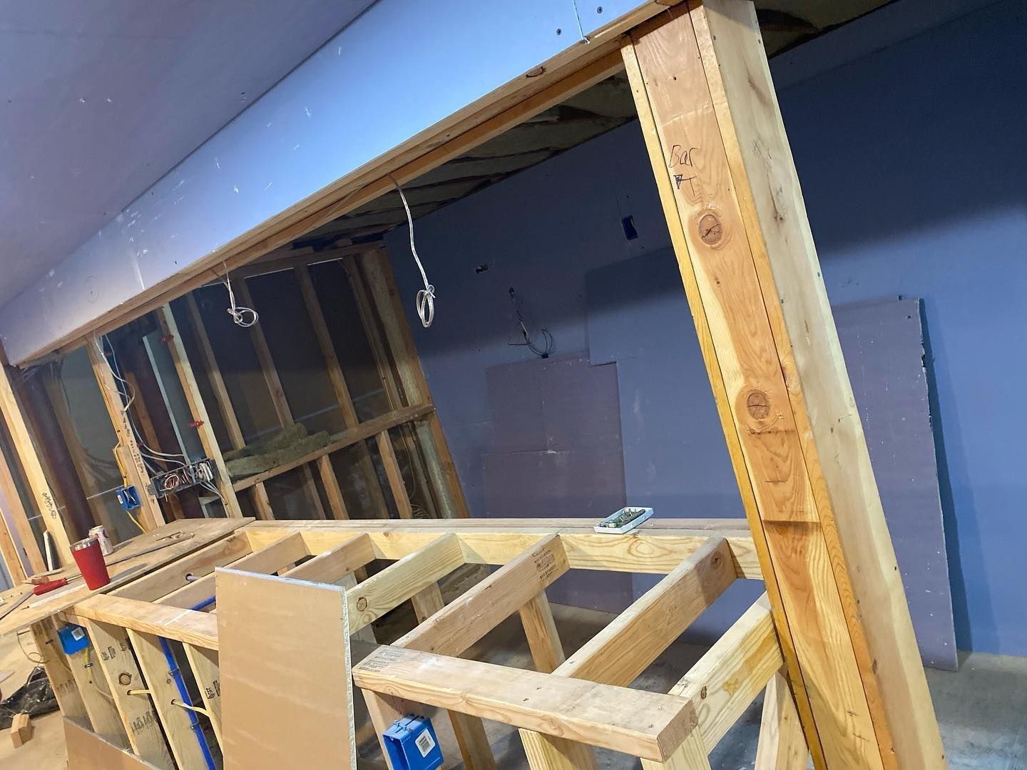 Wooden framework of a construction project with exposed studs, wiring, and drywall. Blue walls and ceiling.