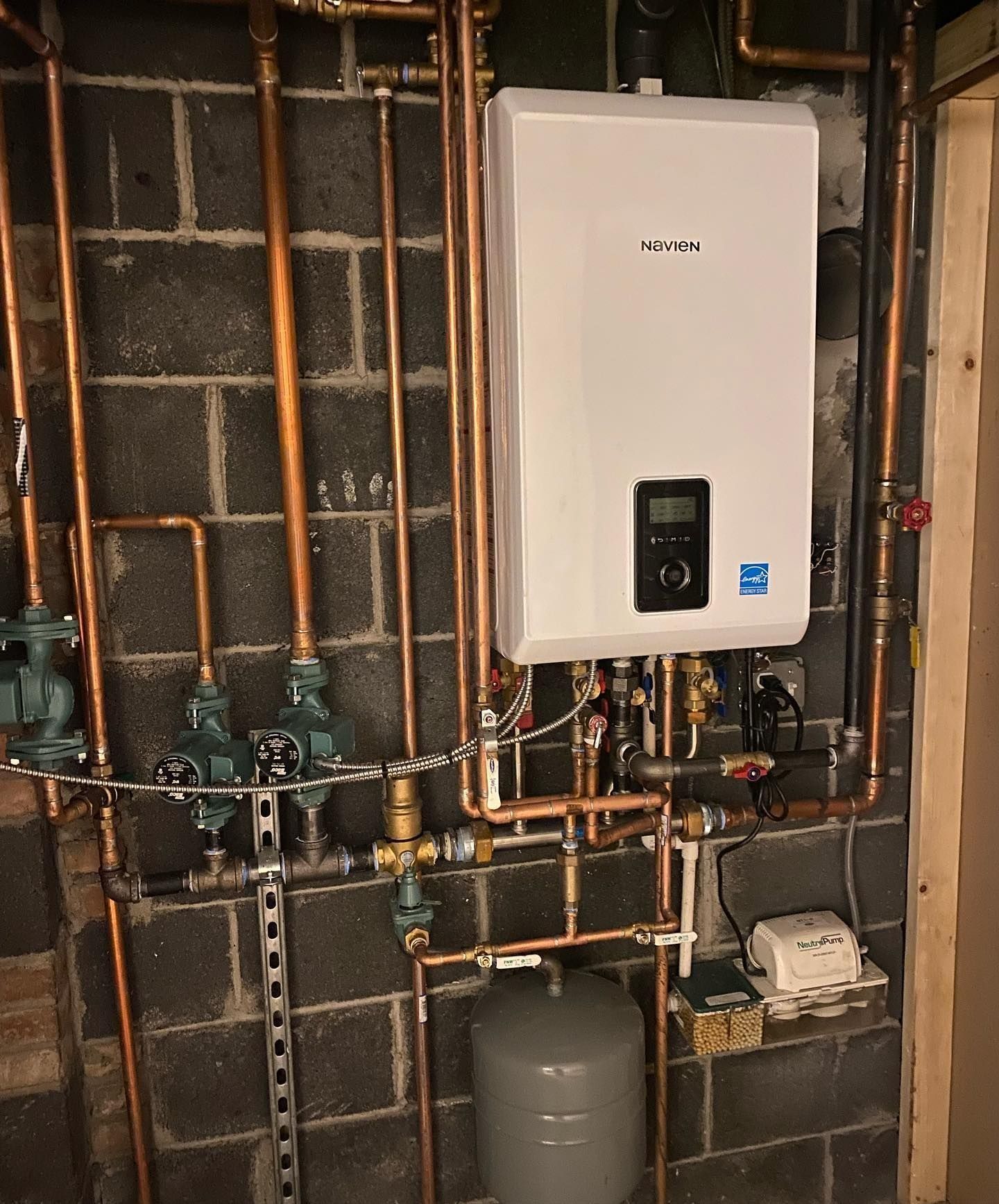 White wall-mounted water heater with copper pipes on a gray cinder block wall.