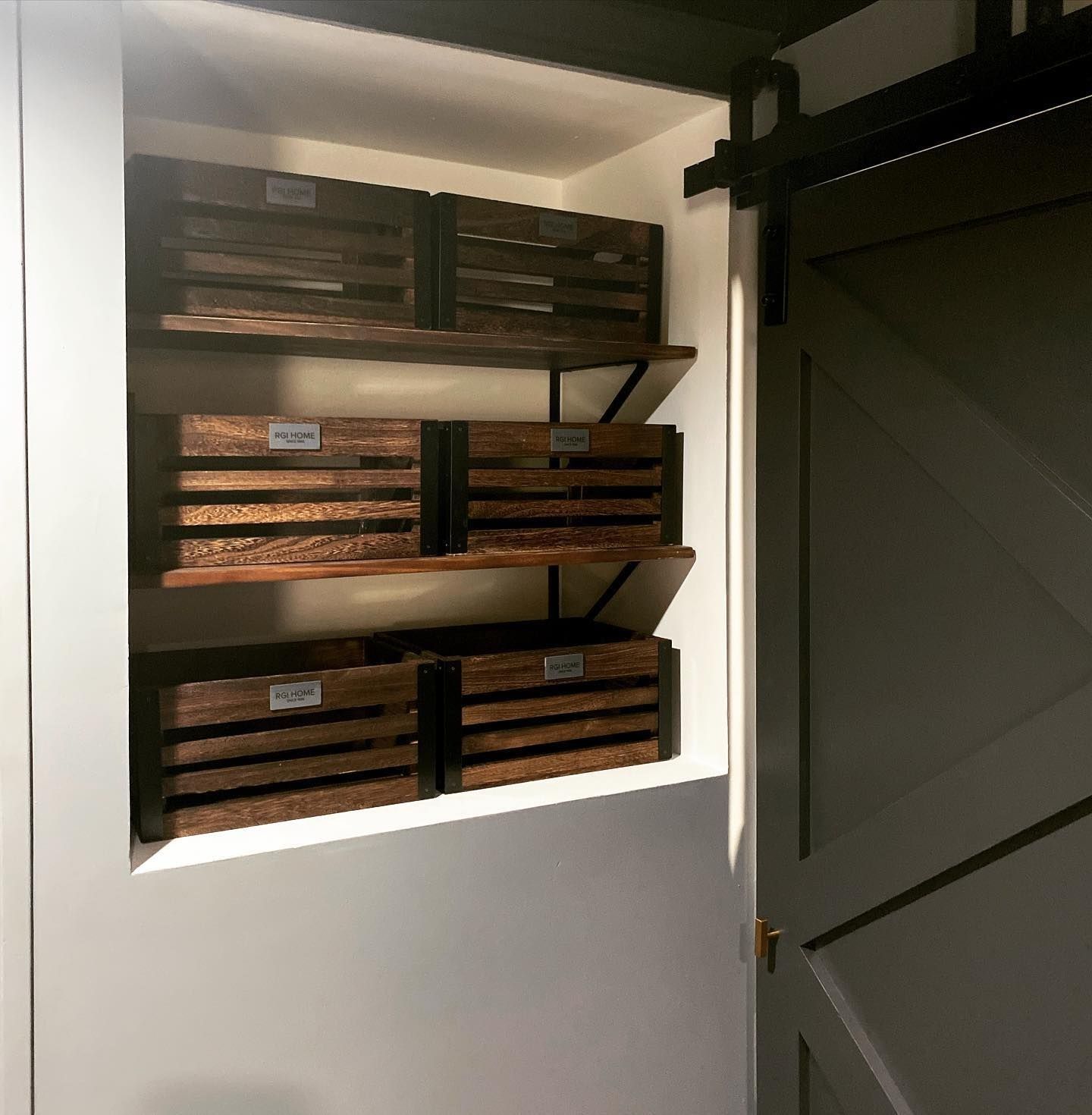 Wooden crates on shelves built into a wall, next to a closed gray sliding barn door.