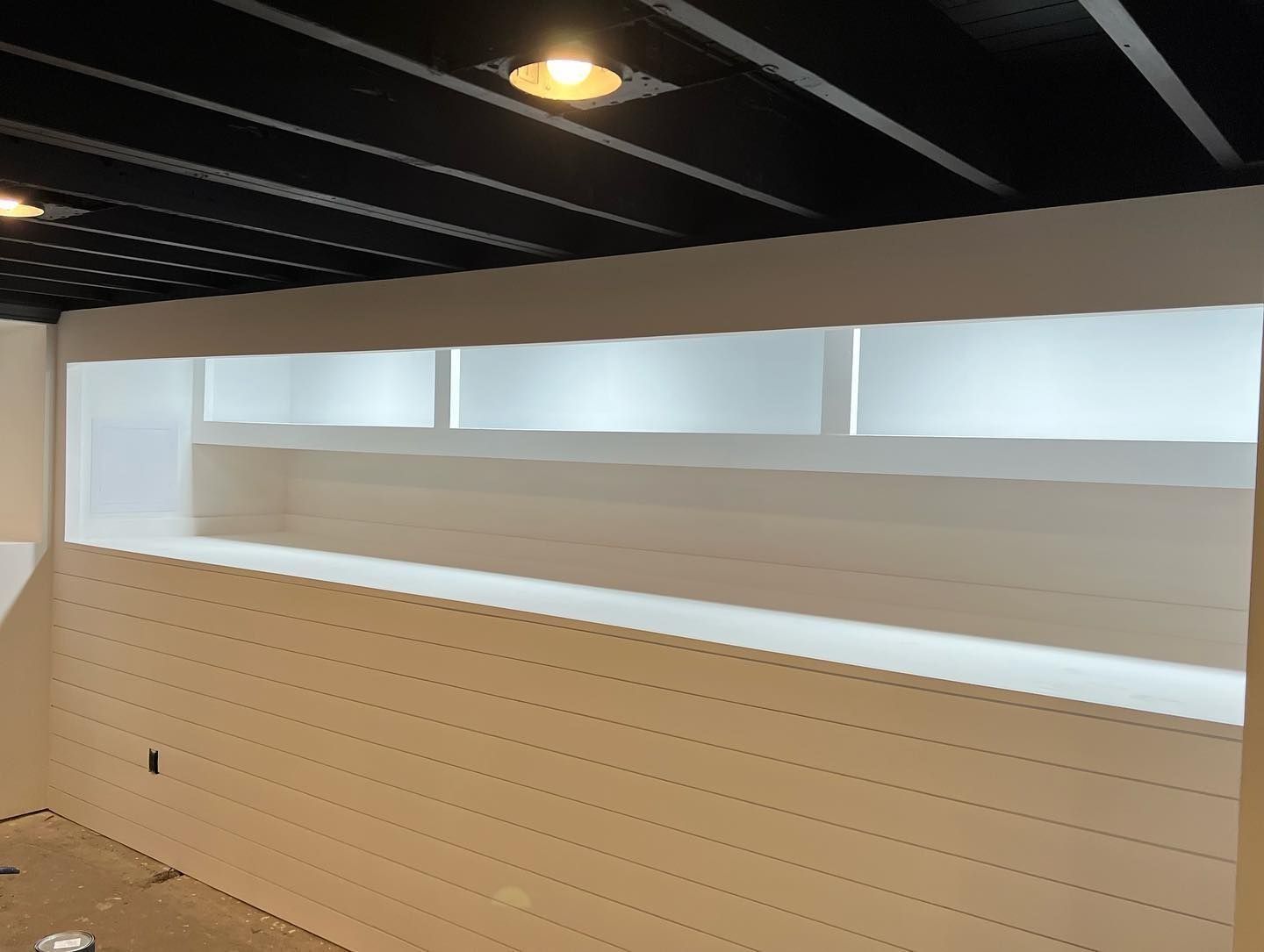 Interior with white shiplap walls, black ceiling. Long horizontal shelf with diffused light above.