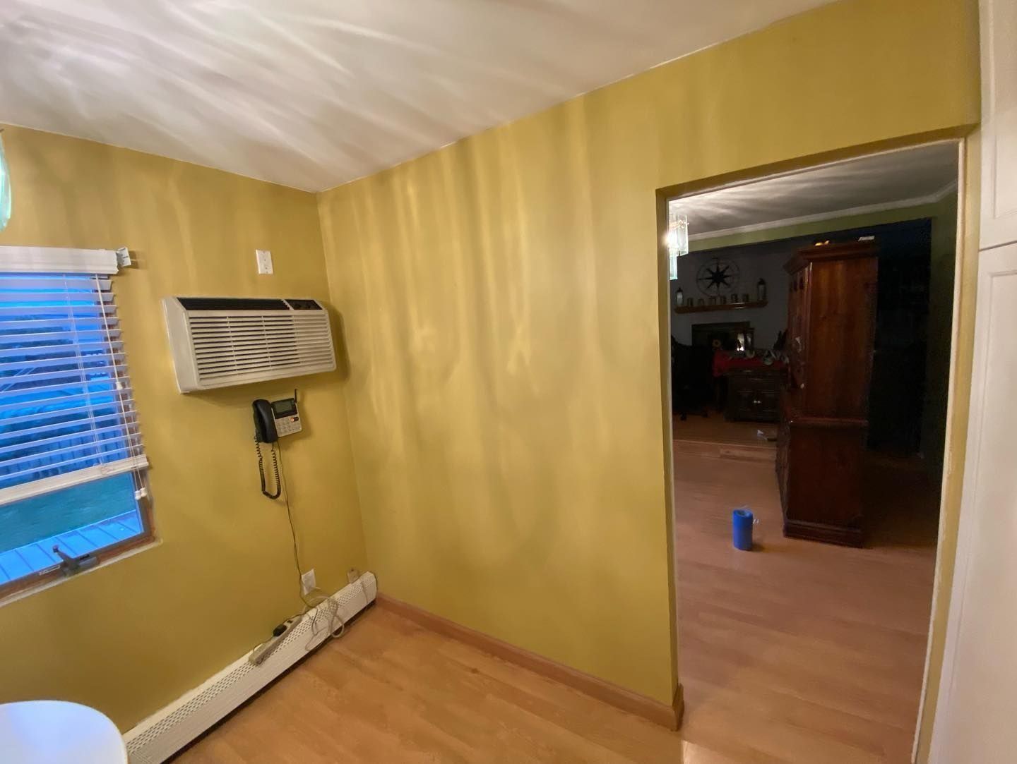 A room with yellow walls, a window AC unit, and an opening to another room.