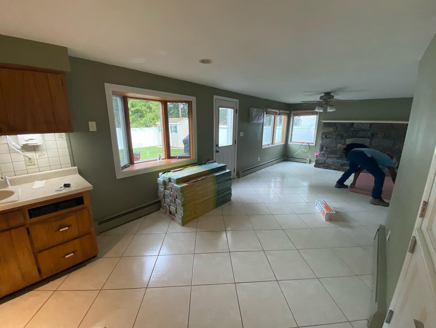 An interior room being renovated with a worker and stacked flooring tiles.