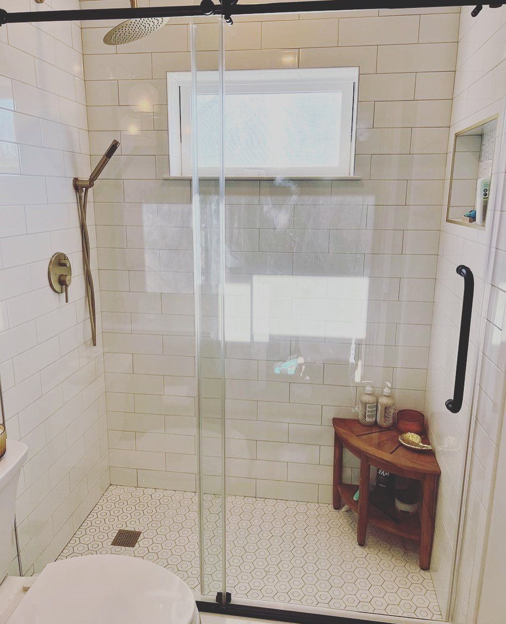 Shower with white tile, glass door, and pebble floor; small wooden shelf.