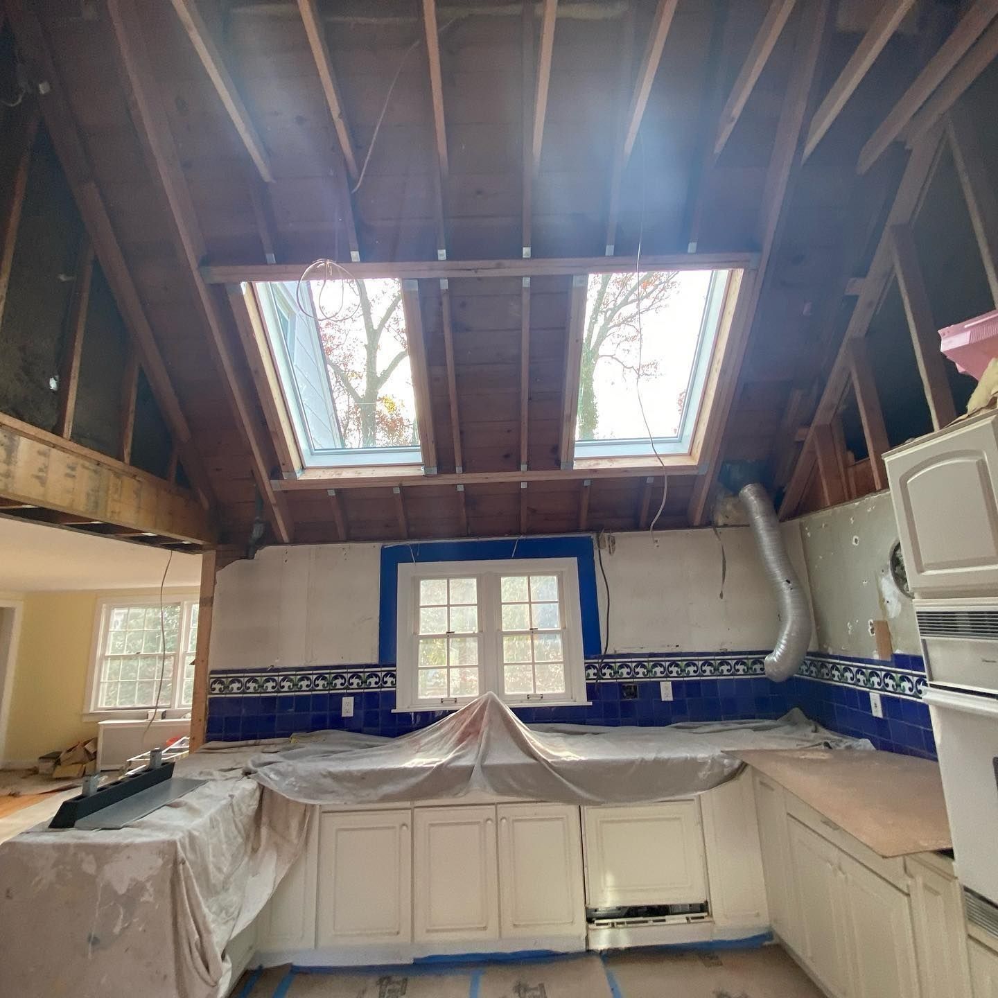Kitchen under renovation, featuring exposed beams, skylights, blue tile, and covered cabinetry.