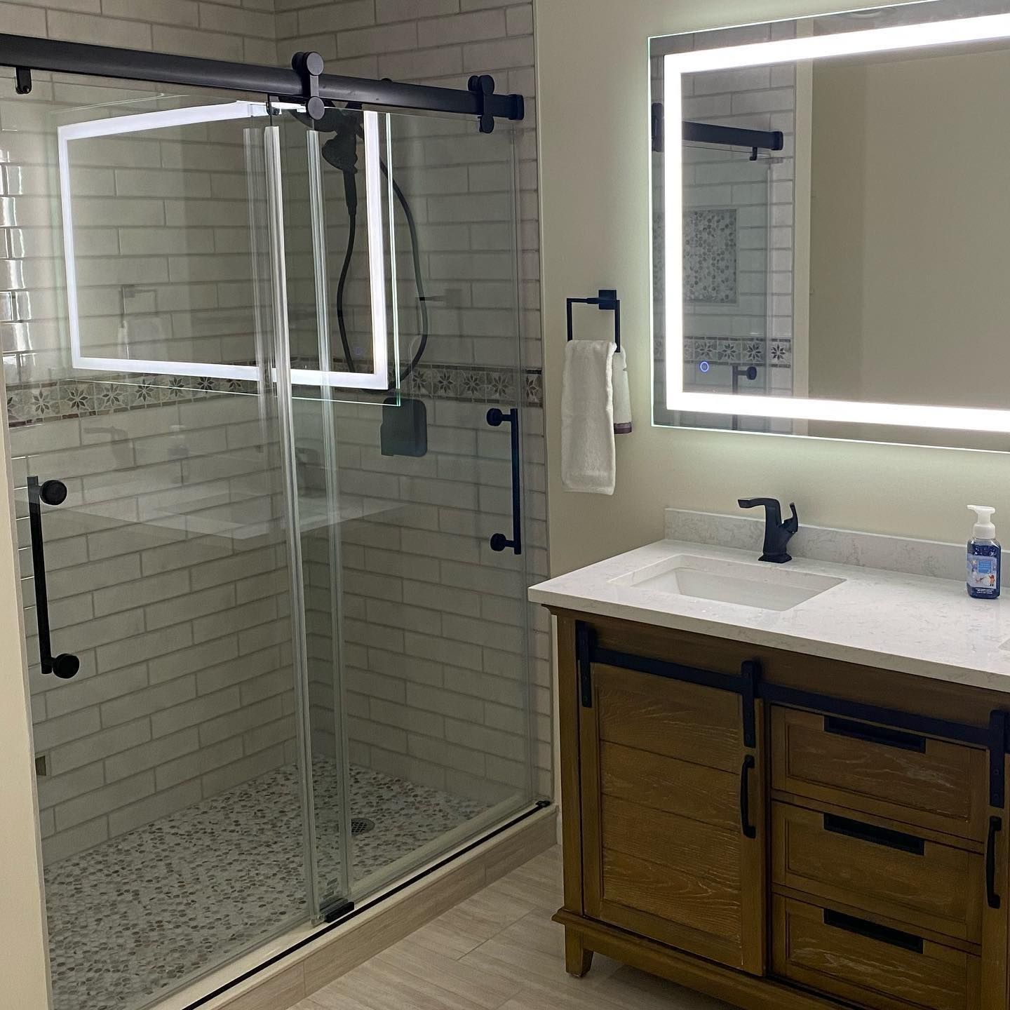 Bathroom with sliding glass shower, wooden vanity, and lit mirror.