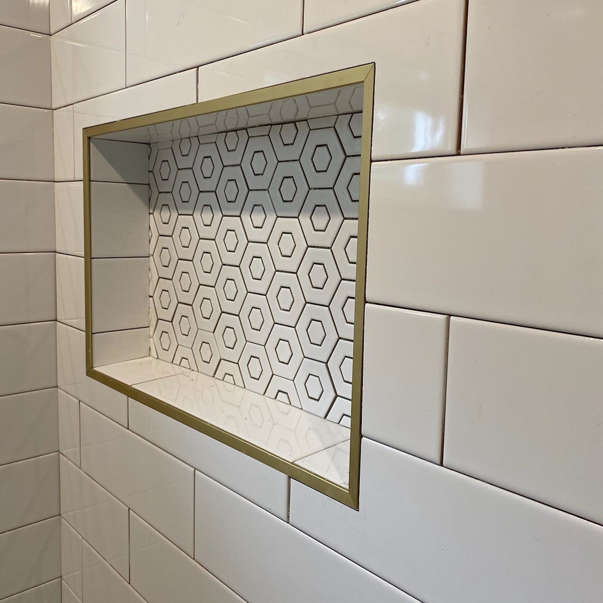 Shower niche with white and hexagon tile, framed in gold.