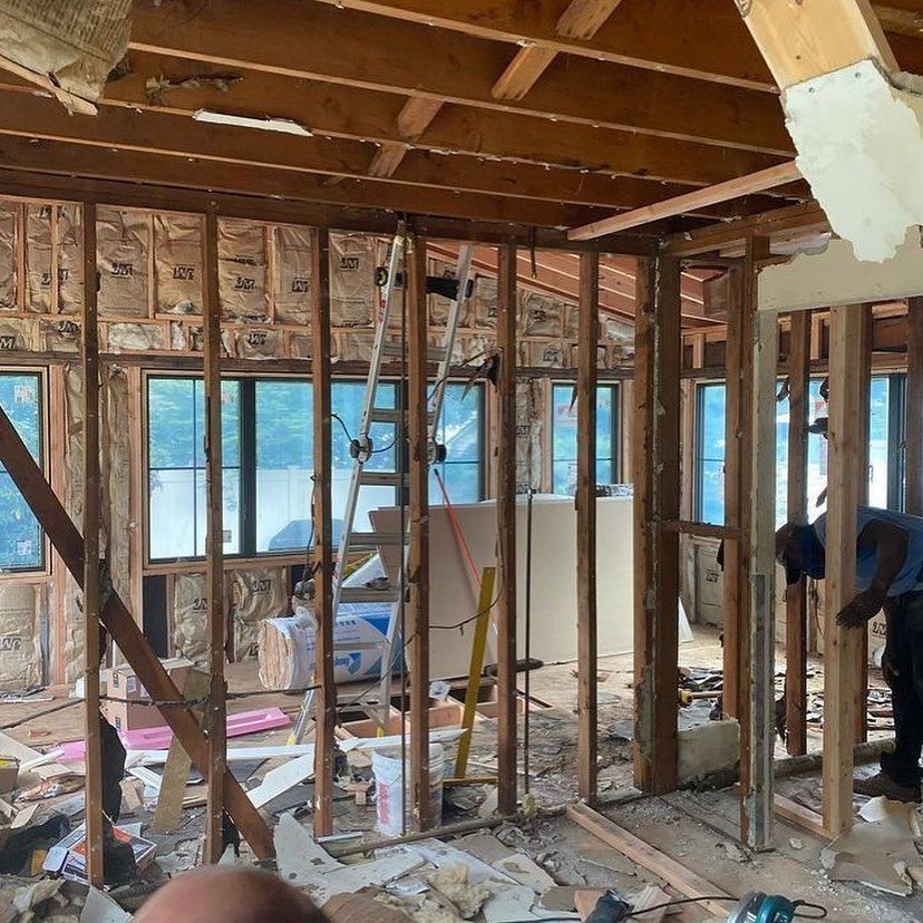 Interior demolition: framing exposed, insulation visible, workers inside, ladder present.