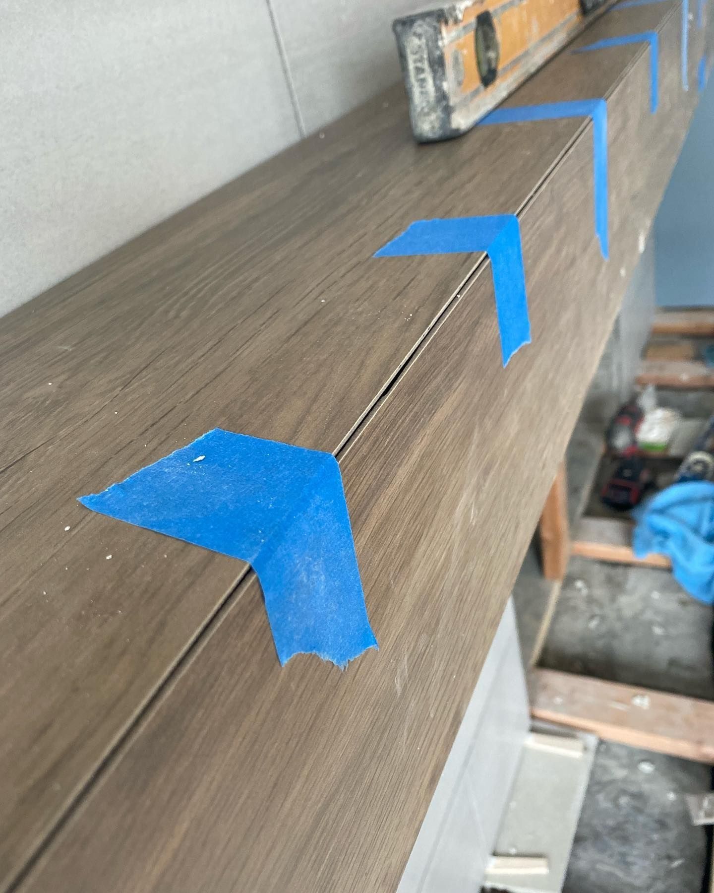 Close-up of tile work in progress, with blue tape marking corners and a level in the background.