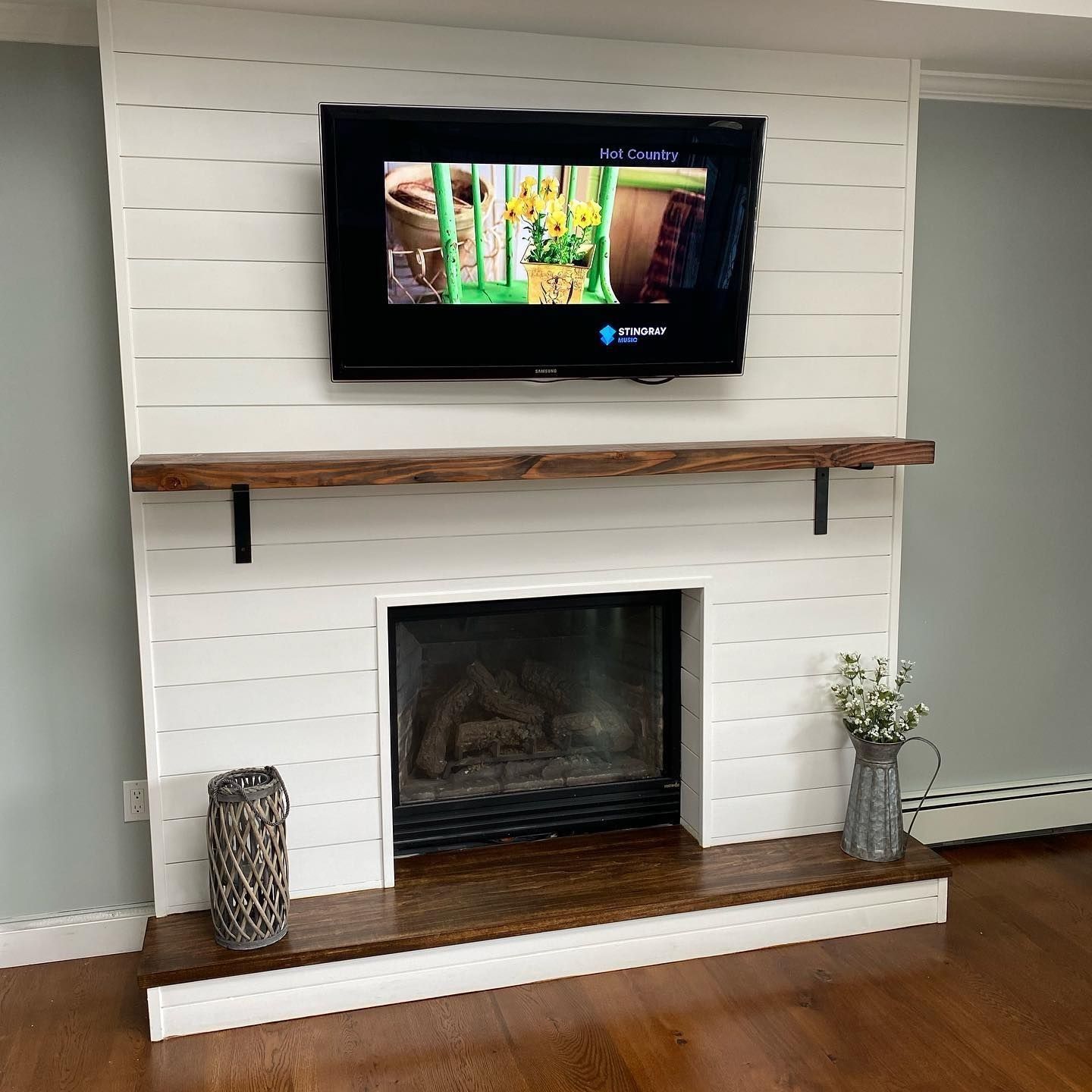 A white shiplap fireplace with a mounted TV, a wooden mantle, and decor on the hearth.