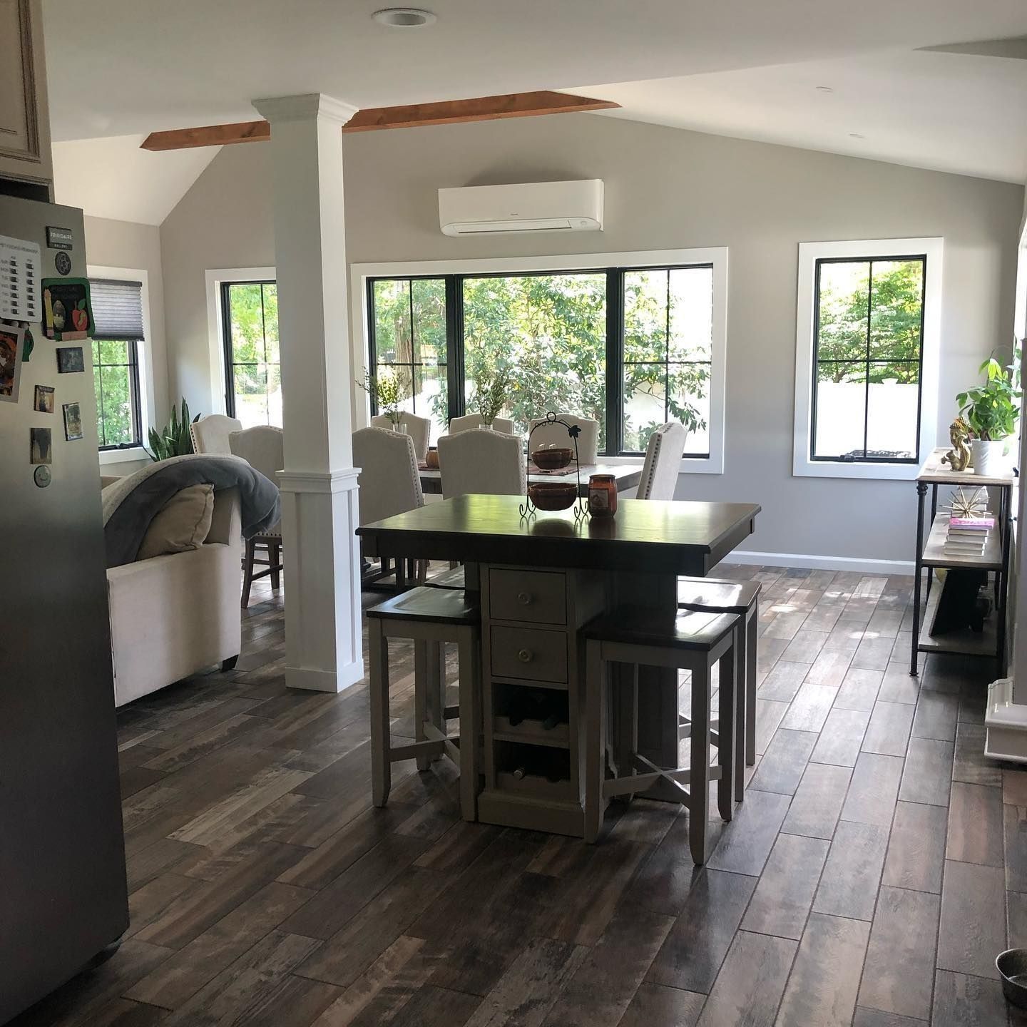 Open-concept kitchen with island and dining area; dark wood floors, white trim, gray walls, and large windows.