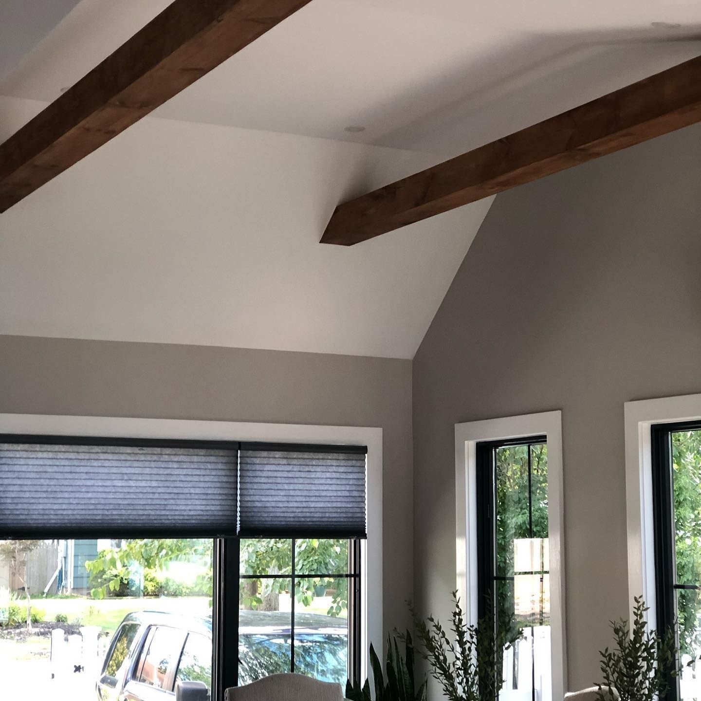 Room interior with white ceiling, wood beams, gray walls, and dark window shades.