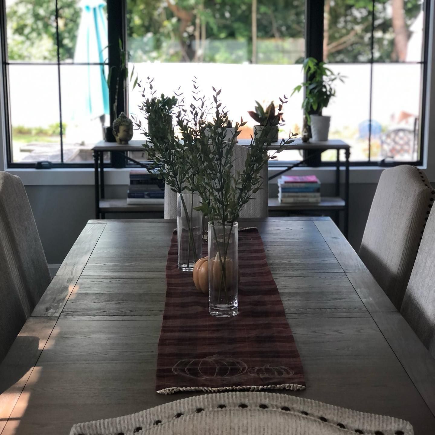 Dining room table set for meal, with center runner, vases, and outdoor view through windows.