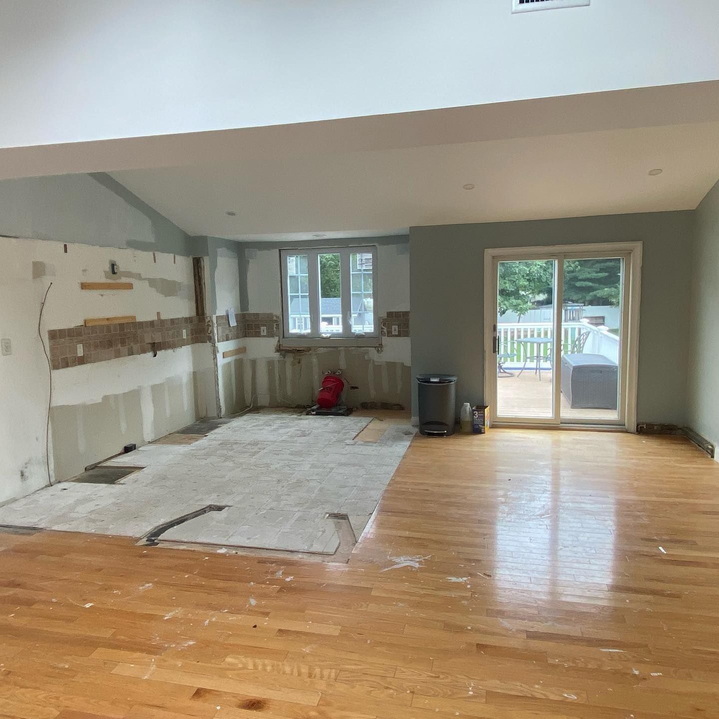 Interior room undergoing renovation, with exposed walls, wood flooring, and a sliding glass door.