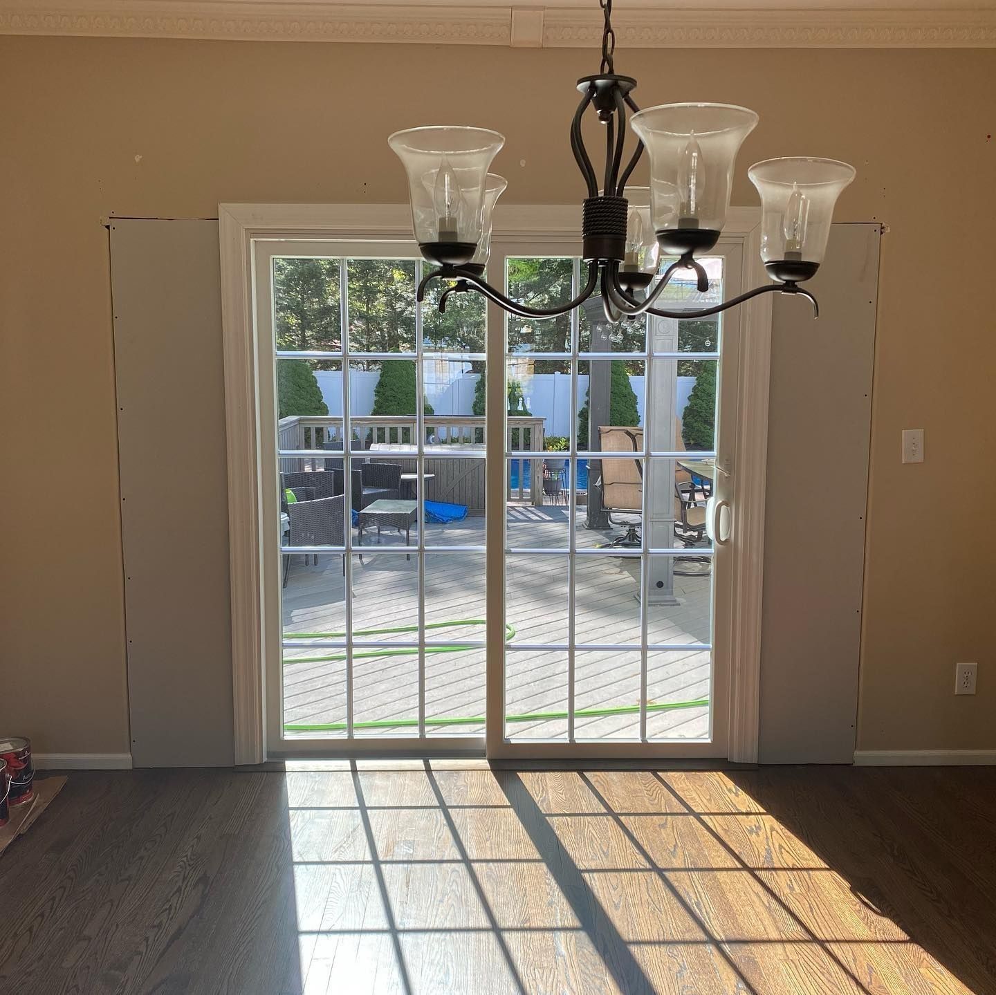 Dining room with sliding glass doors, chandelier, and sunlight casting shadows on wood floor.