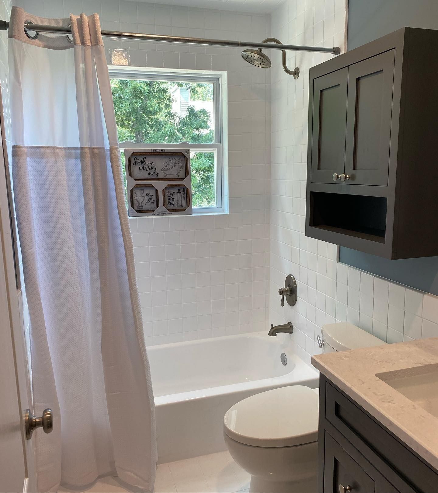 Bathroom with white tile, a tub, and a gray vanity and cabinet. Shower curtain is closed.