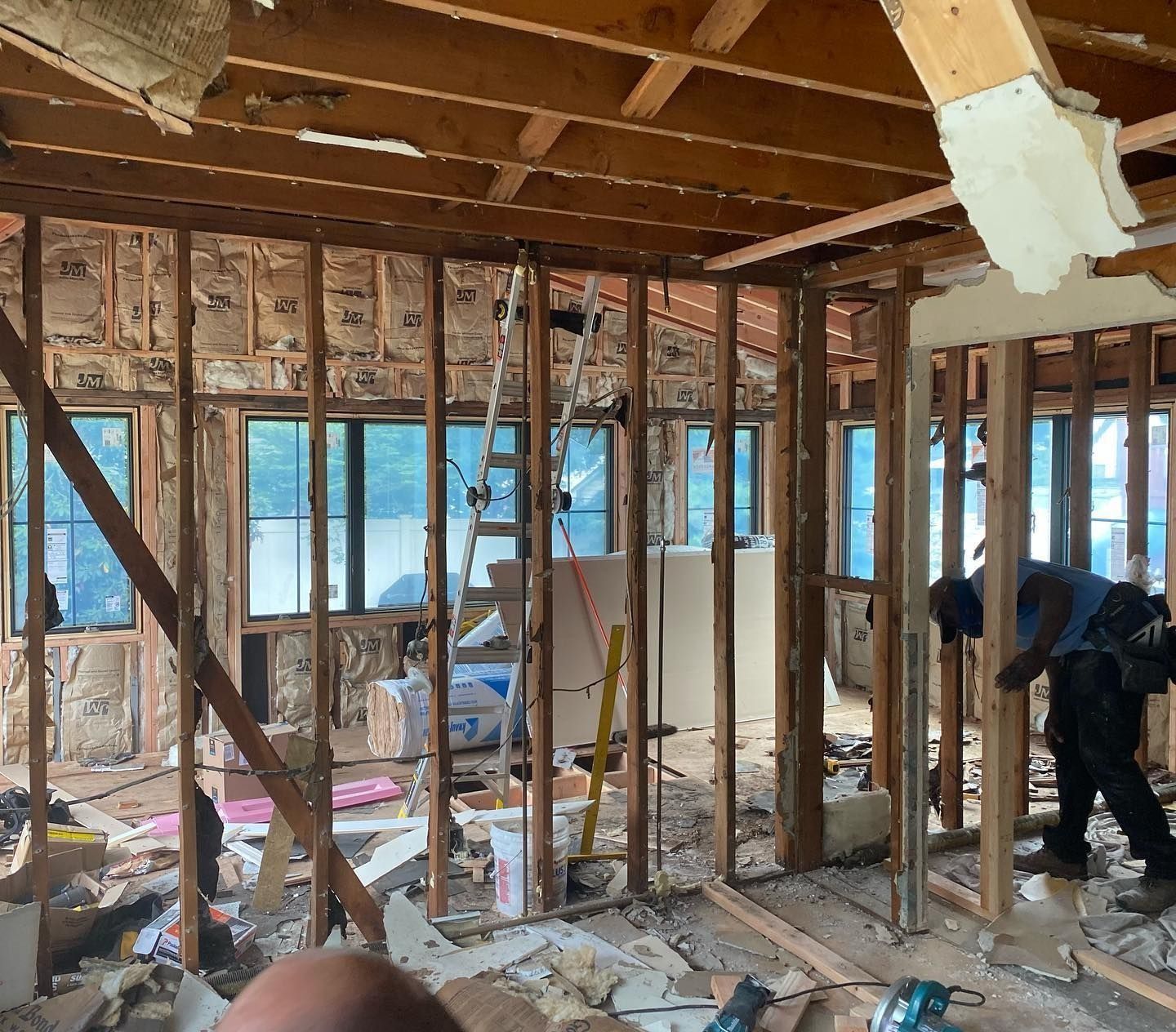 Interior of a building under renovation, exposed wooden framing, ladder, drywall, workers present.