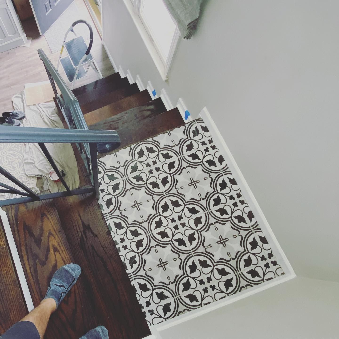 Staircase with patterned tile landing, dark wood steps, white trim, and a handrail. A person's feet are visible.