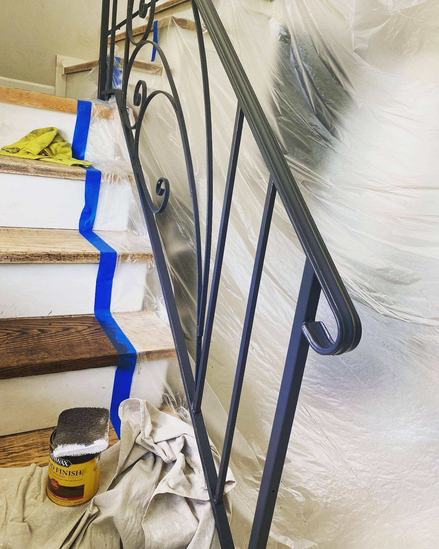 Staircase with black metal railing, taped for painting. Protective plastic covers surrounding area.