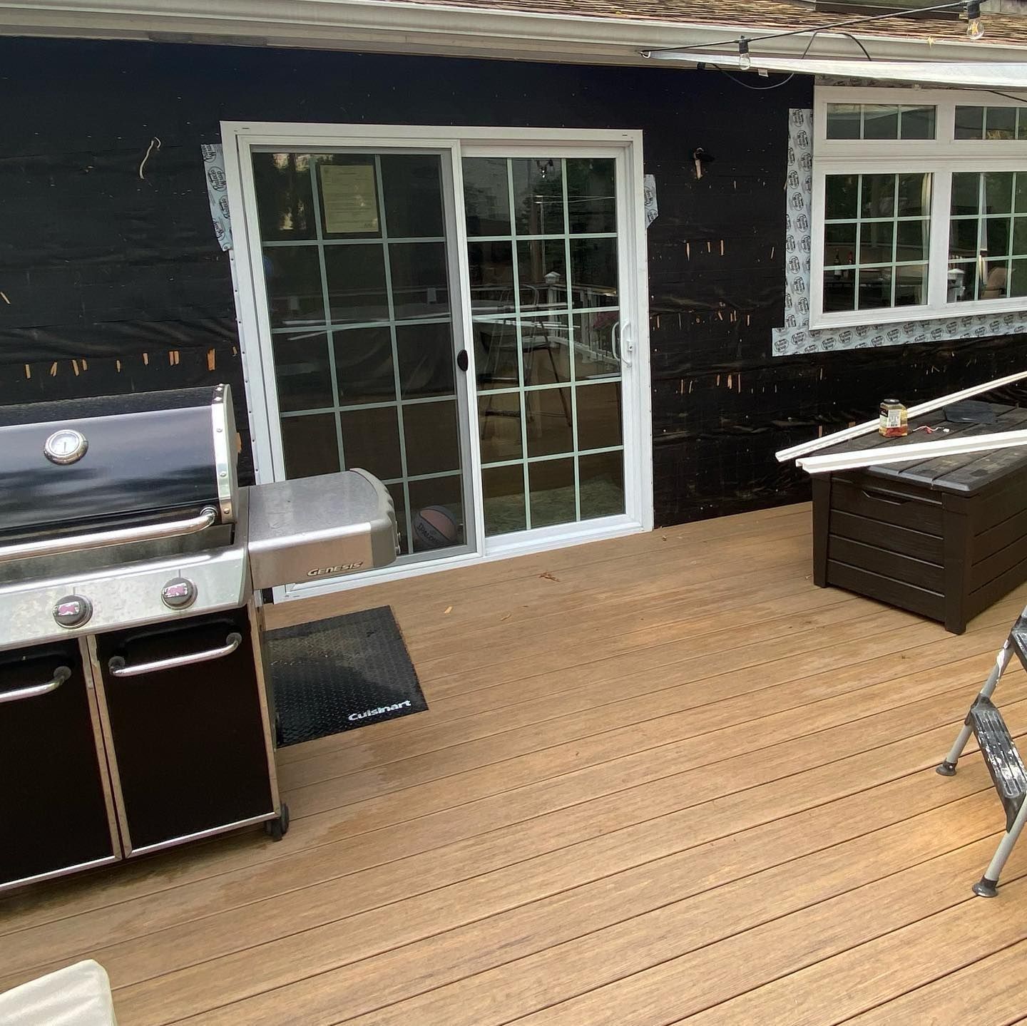 Composite deck with grill, sliding door, and window. Black house wrap visible.