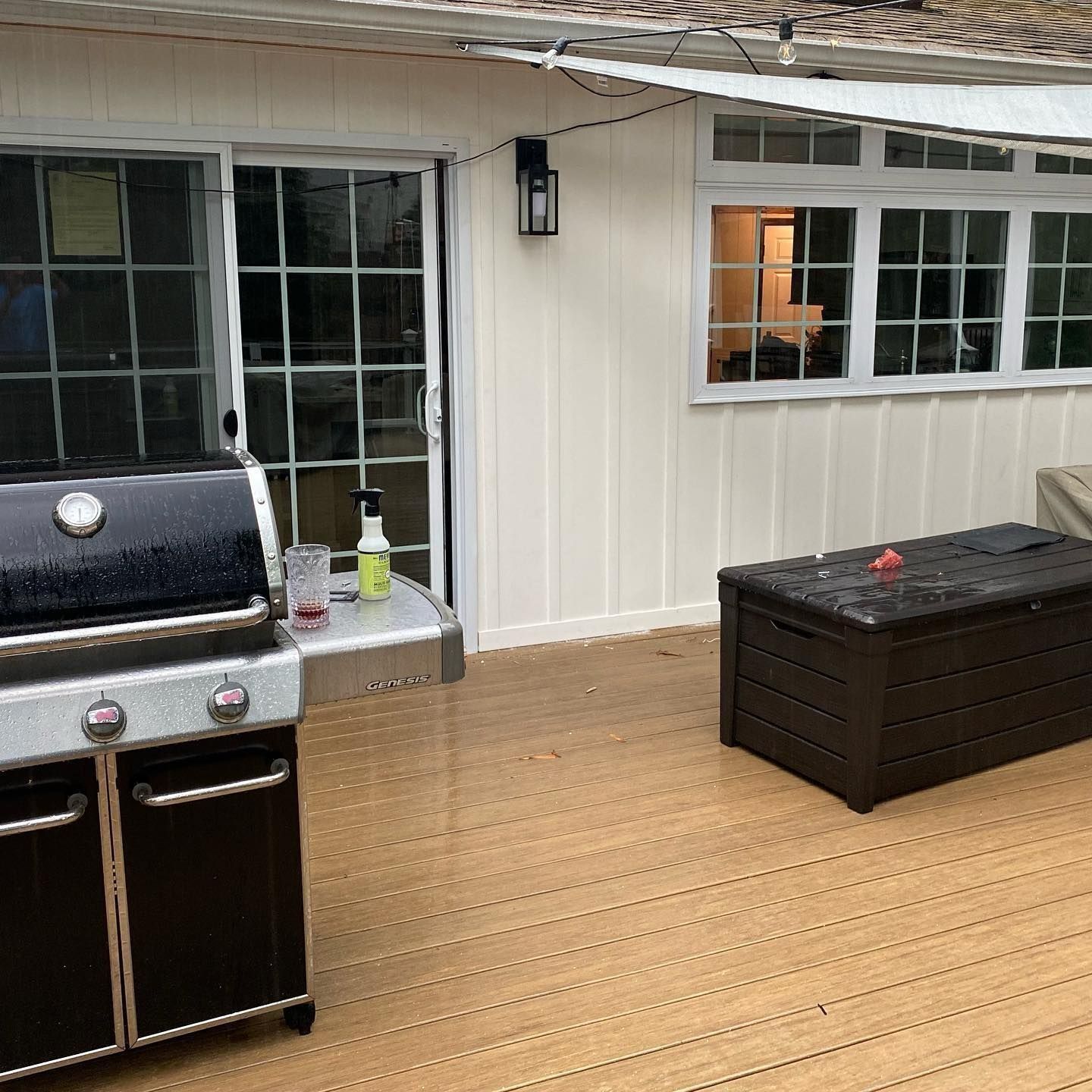 Patio with grill, sliding glass door, and brown storage box on a wooden deck.